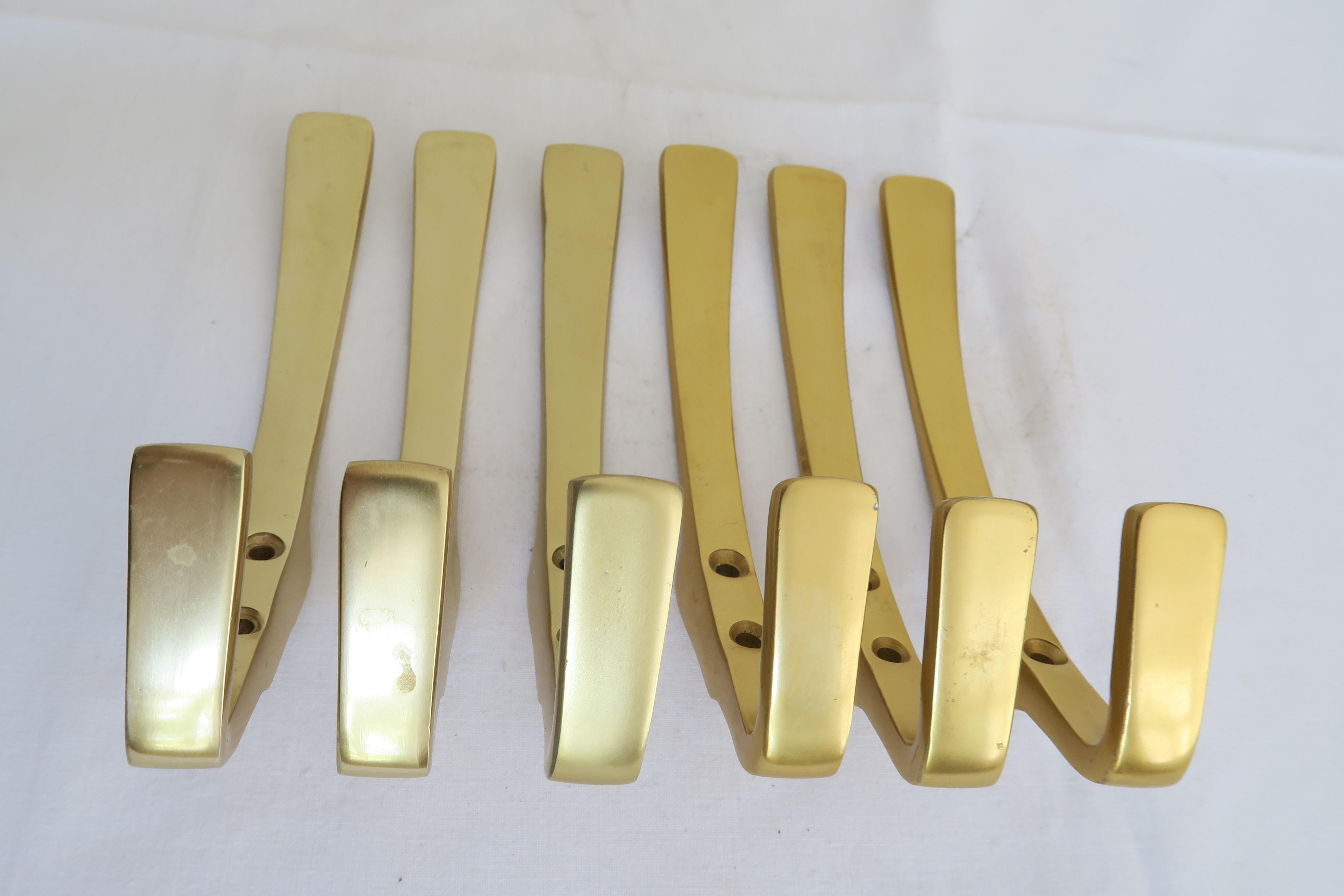 For sale is a set of 6 gold-colored aluminum coat hooks. The hooks can be wall mounted and are similar in style to Carl Auböcks designs. Half of the hooks are a slightly more warm gold tone than the other half, so they could either be mounted