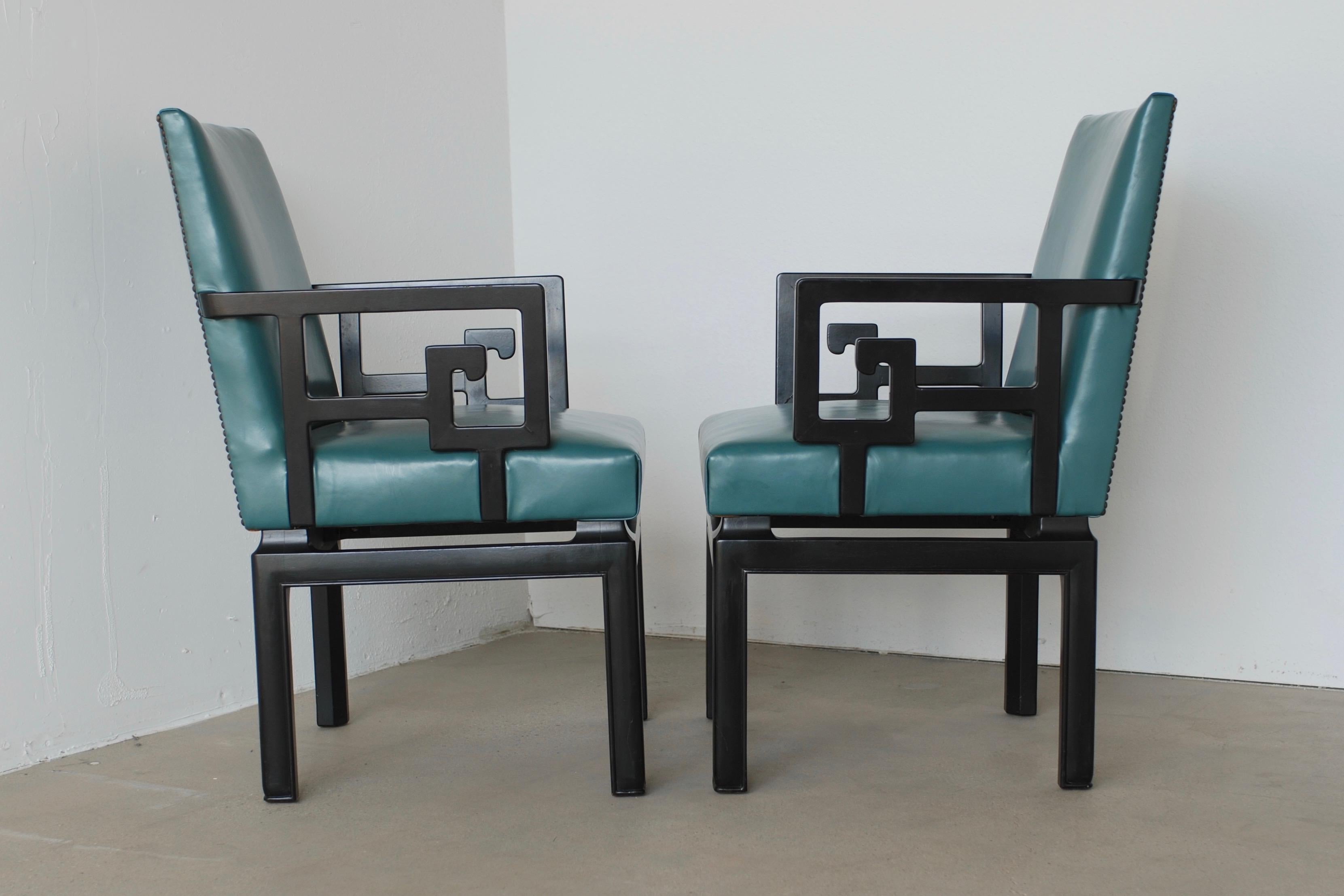 These teal or turquoise colored leather and ebony black lacquered wood dining chairs by Baker are attributed to Michael Taylor. The captains chairs have a greek key pattern and the four side chairs are armless. The chairs retain their original Baker