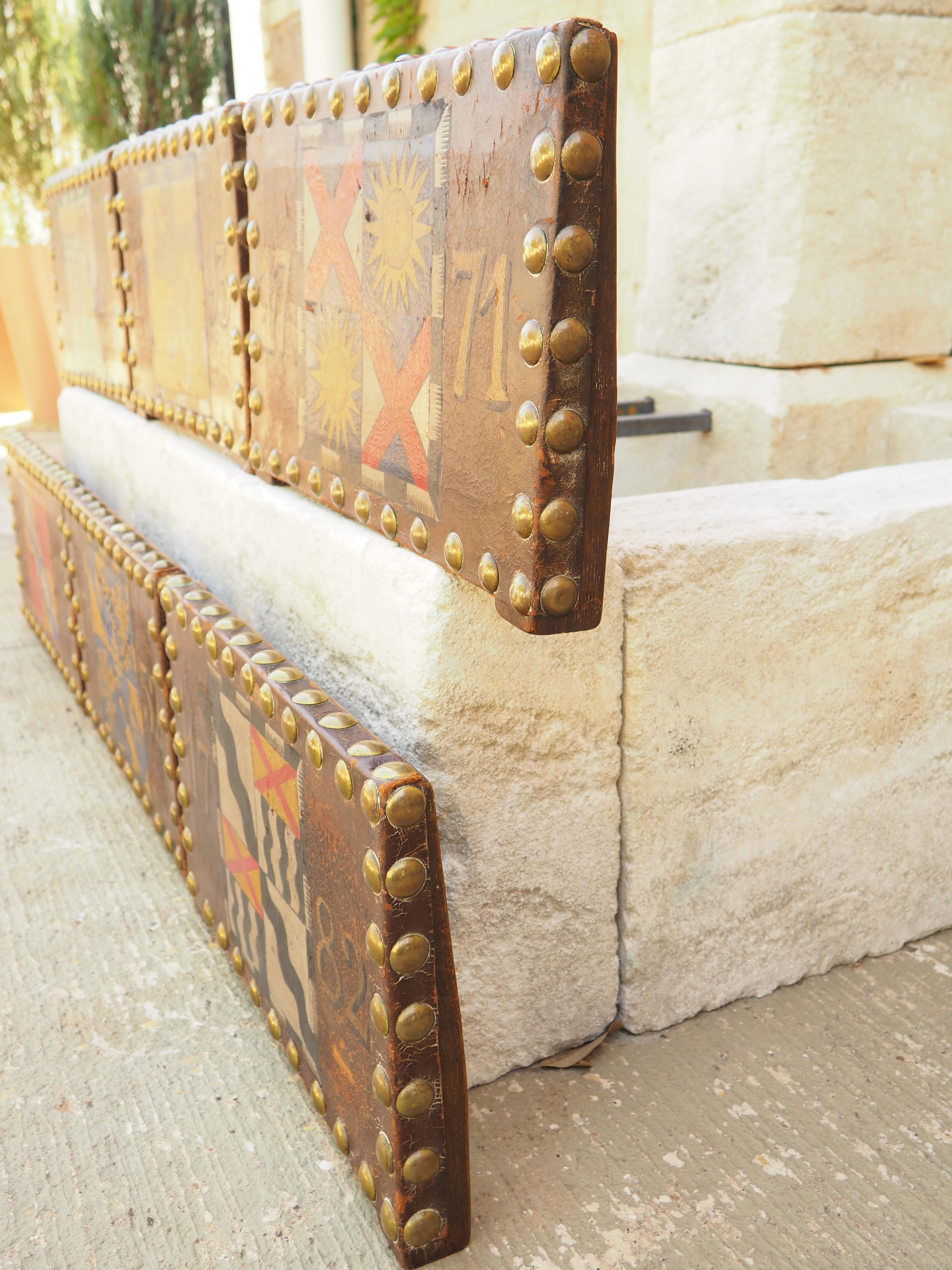 Originally the backrests to a set of Spanish leather chairs dating to around the 1880s, these studded chair backs have been painted more recently with dated heraldic displays. The chocolate-colored leather is dotted by numerous brass nailheads that