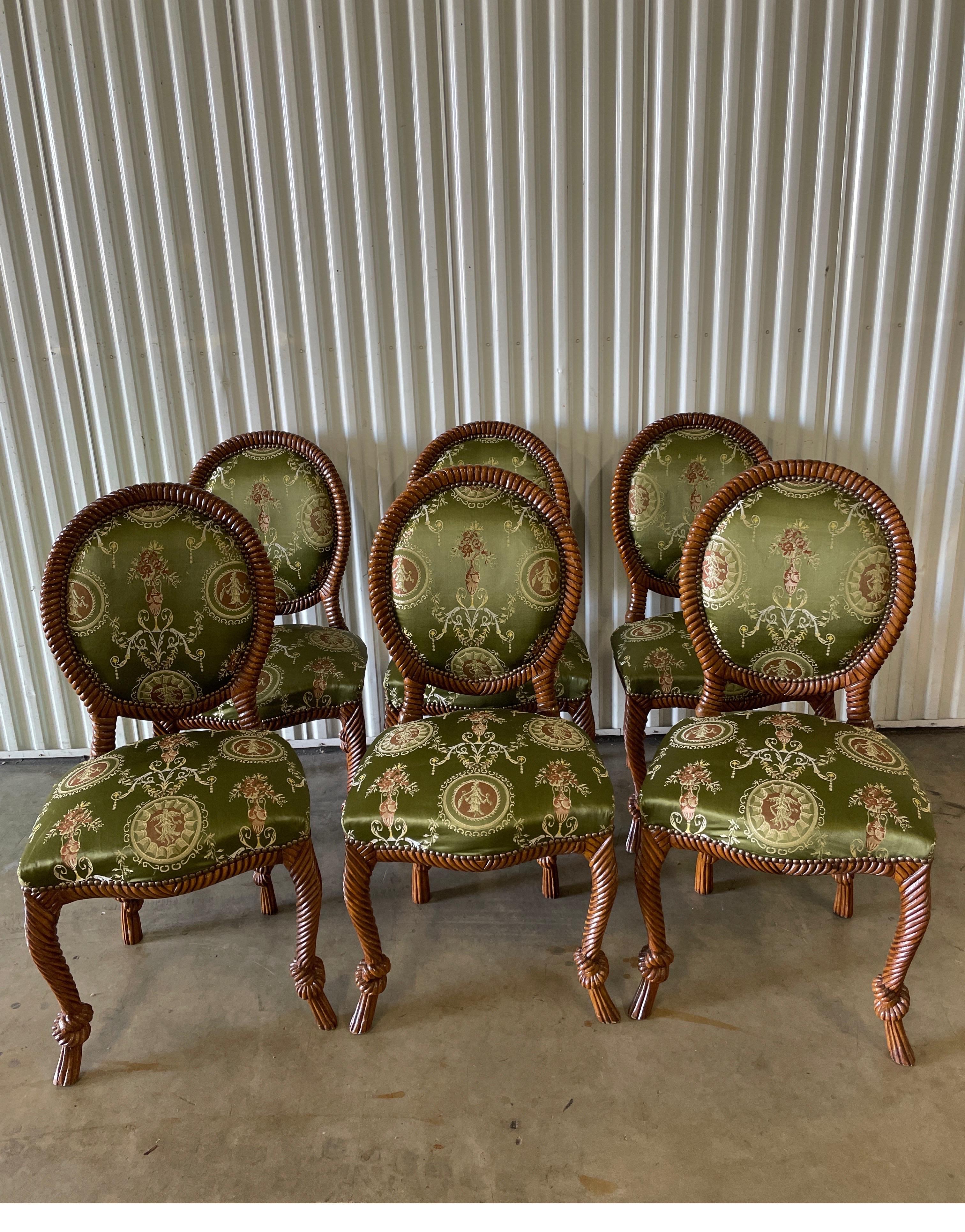 Set of six Hollywood Regency dining room chairs in the rope & tassel style wood frame. These glamourous chairs will definitely make your dining room sparkle. Upholstered in a European silk fabric with nail head surrounds.