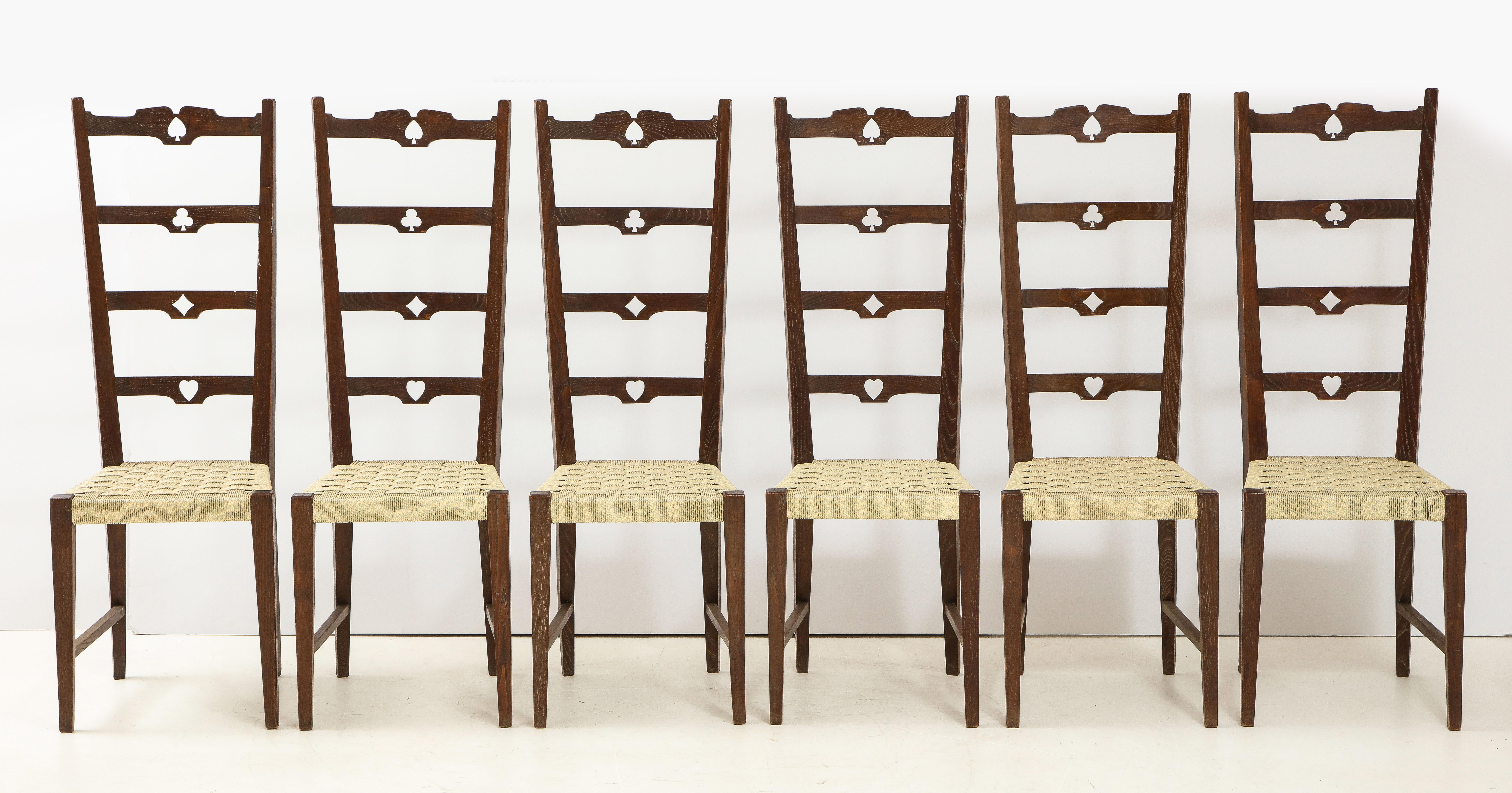 Very unique Italian rustic set of six walnut ladder back chairs; the back slats decorated with carved motifs of the four playing card symbols: clubs (?), diamonds (?), hearts (?), and spades (?). The seats covered in faux straw; the chairs are
