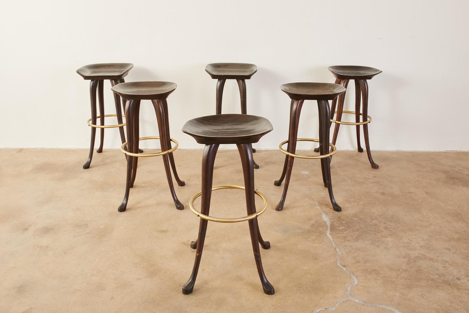 Rare set of six carved bar height stools handcrafted by Jean of Topanga California. The stools feature a carved saddle style seat supported by elegant, long legs ending with hoof style feet. The legs are conjoined by a brass toned ring stretcher