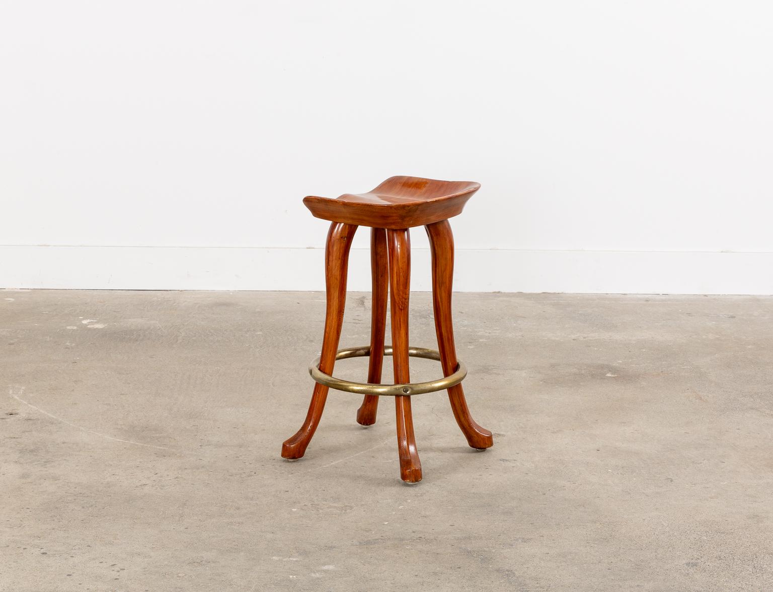 Rare set of six carved counter height bar stools handcrafted by Jean of Topanga California. The stools feature a carved saddle style seat supported by elegant legs ending with a hoof-style foot. The legs are conjoined by a brass toned ring stretcher