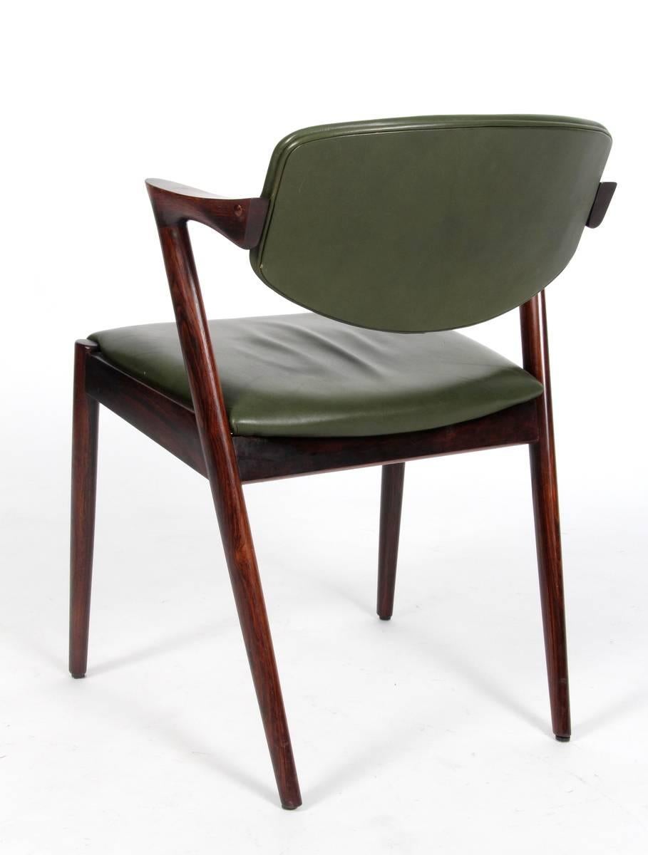 Dining chairs, model 42, designed by Kai Kristiansen and manufactured in Denmark by Schou Andersen Møbelfabrik. The chairs are made from solid rosewood, featuring tapered legs, curved armrests and green leather upholstery. Good vintage condition.
 