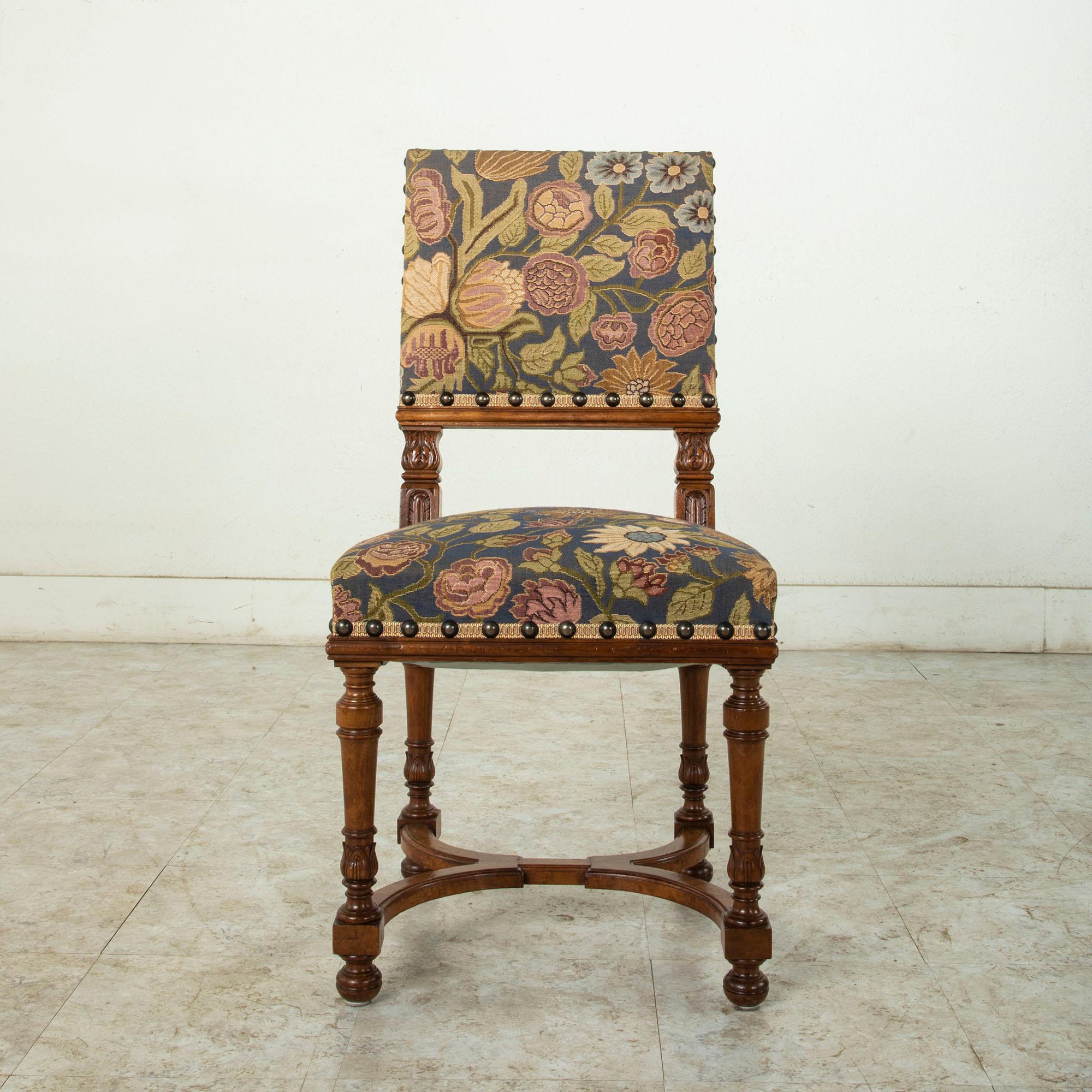 This set of six French Henri II style walnut side chairs or dining chairs features hand carved details of leaves on the seat back and turned legs. A curved X-stretcher between the legs provides stability. The chairs are upholstered in tapestry with