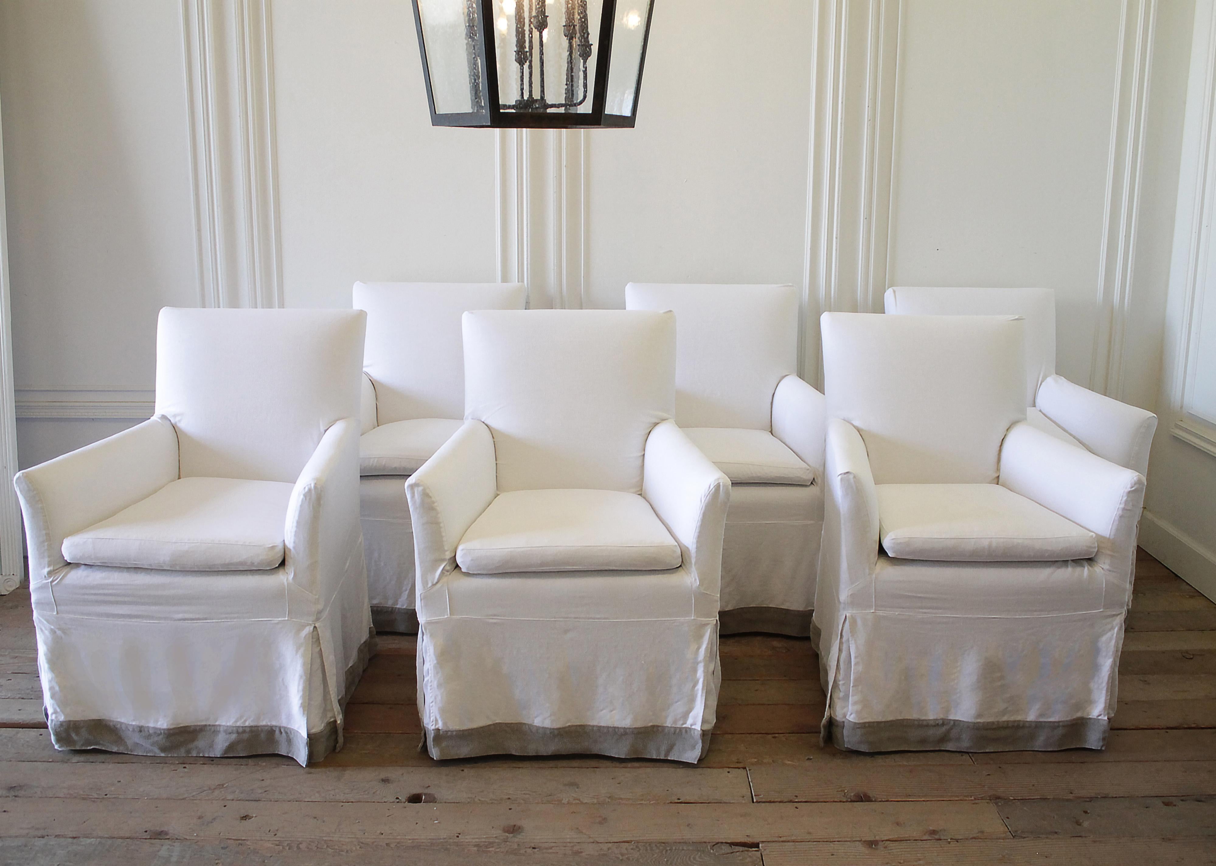 Set of six canvas upholstered arm chairs, with decorative wood legs. Slip covers done in white heavier weight Belgian linen in soft white. We added a decorative accent in natural linen at the bottom of the slip covers. 3