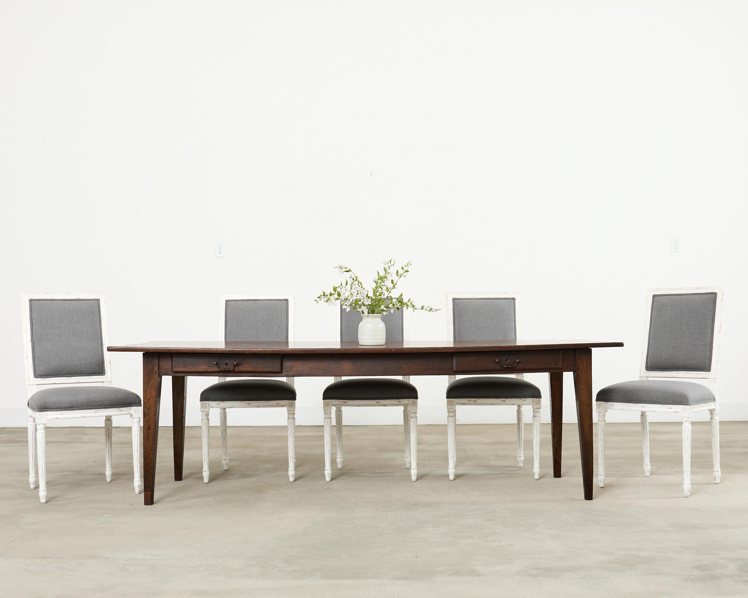 Classic set of six French Louis XVI style painted dining chairs having a distinctive square back. The set features a painted finish with an intentionally aged, weathered patina. The beech frames have been reupholstered in the past with a grey