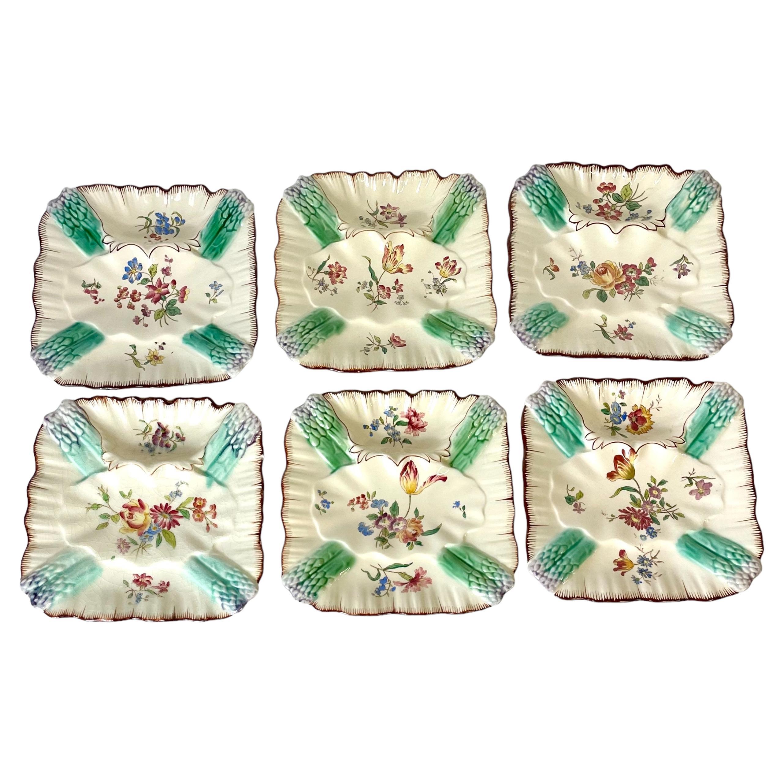 A charming set of six earthenware hand-painted square asparagus plates, with a pair of Majolica glazed asparagus tips at each of the four corners. In between, sprays of polychrome flowers adorn the centre, all set against a beautiful cream glazed