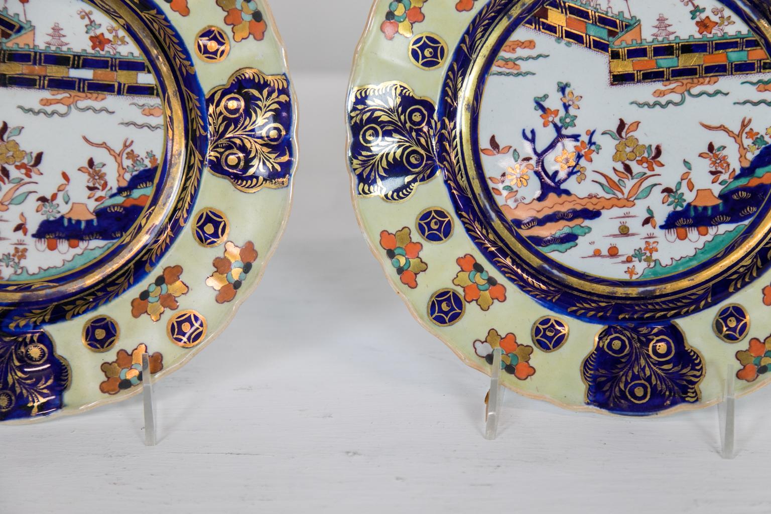 These dinner plates have scalloped edges that frame a border with a rare yellow background containing stylized leaf clusters and round star lozenges interspersed with four cobalt cartouches of gilt leaves. The center panel has a fence pattern and a