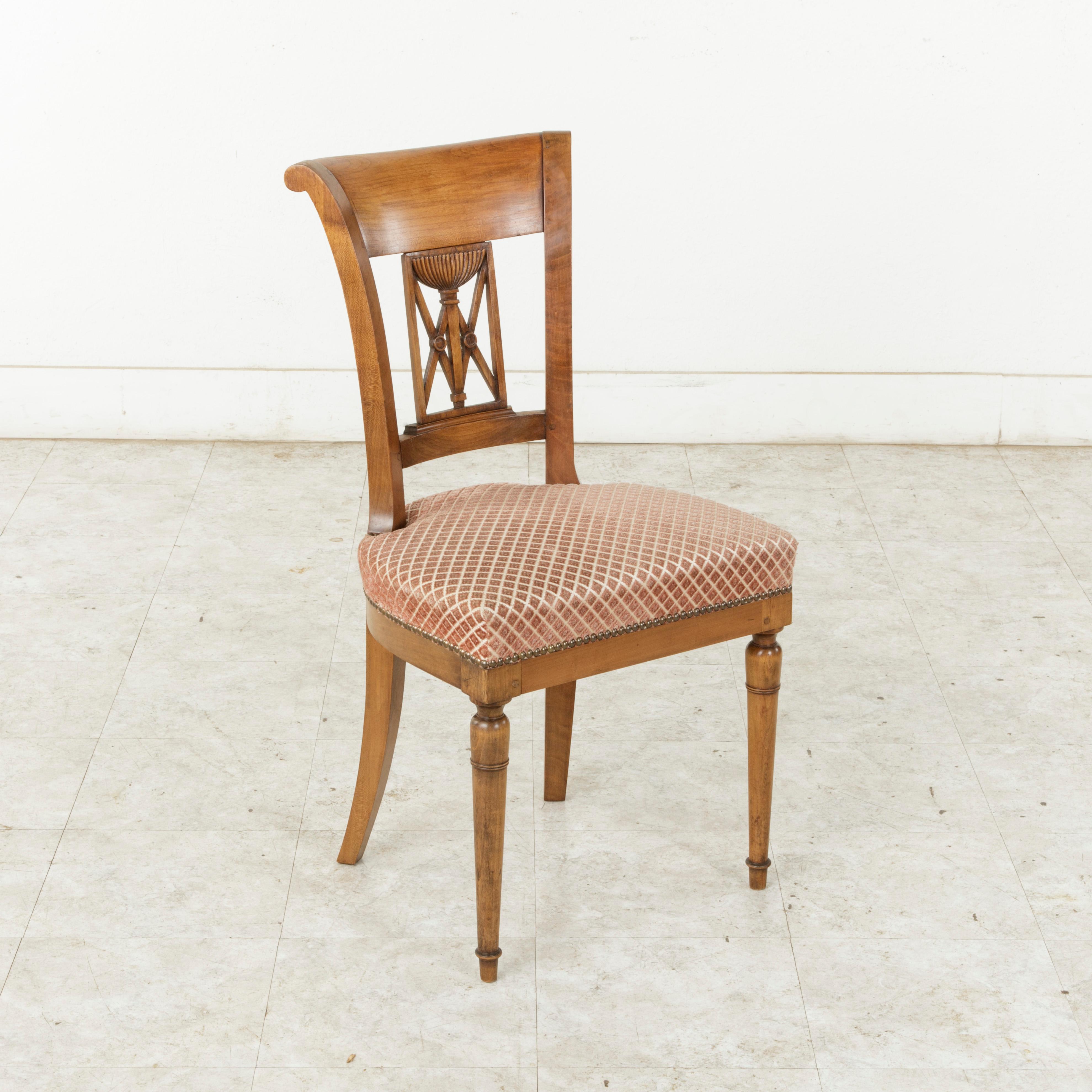 This set of six handsome French Directoire style dining chairs from the mid-20th century are constructed of solid walnut. They feature scrolled seat backs with a hand carved urn and double X motif. The front turned legs are tapered, while the square