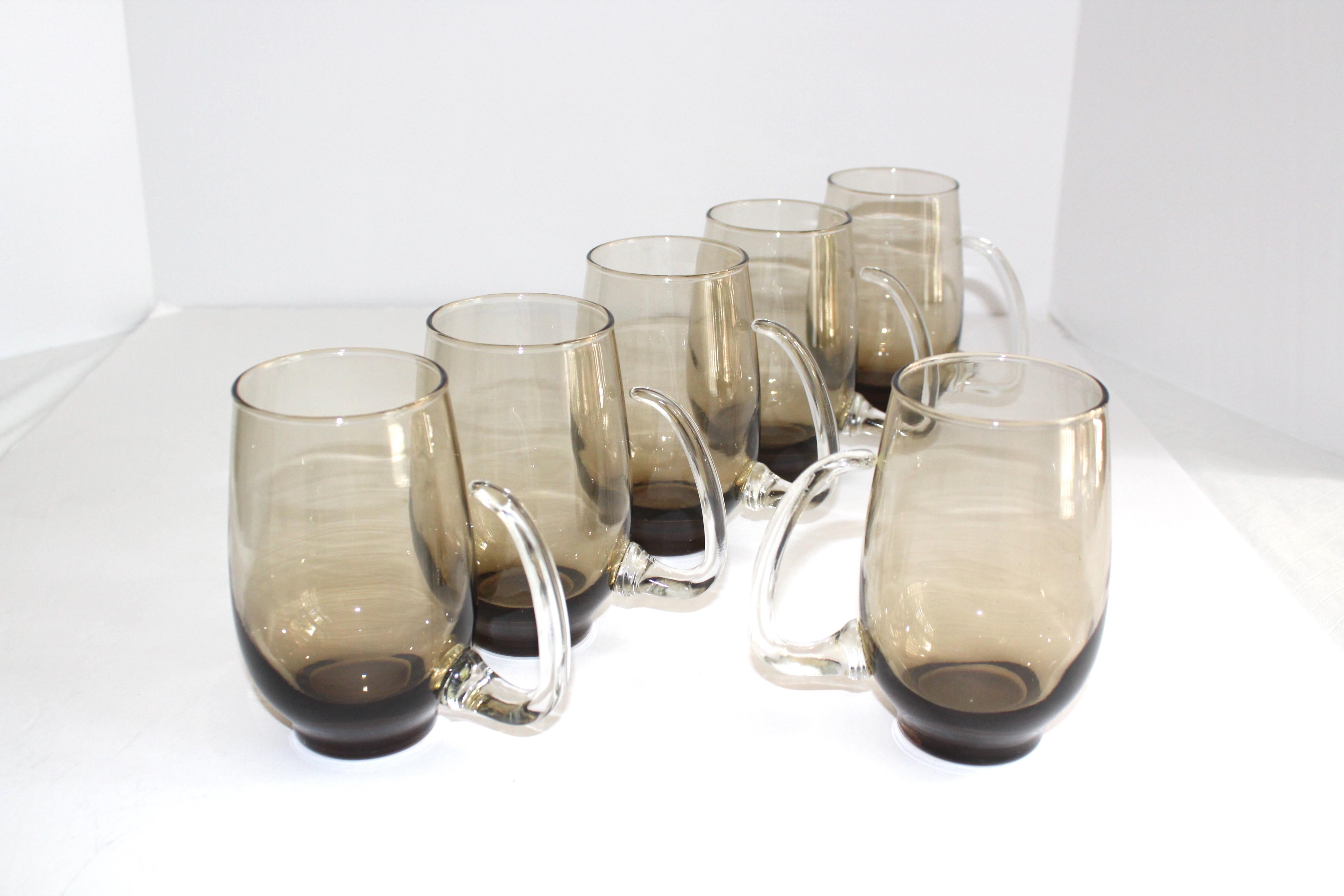 Set of six Mid-Century Modern barware glasses and beer mug. Handblown glass with smokey grey or brown tint. The glasses feature modernist clear glass handles with stylized horn formation.