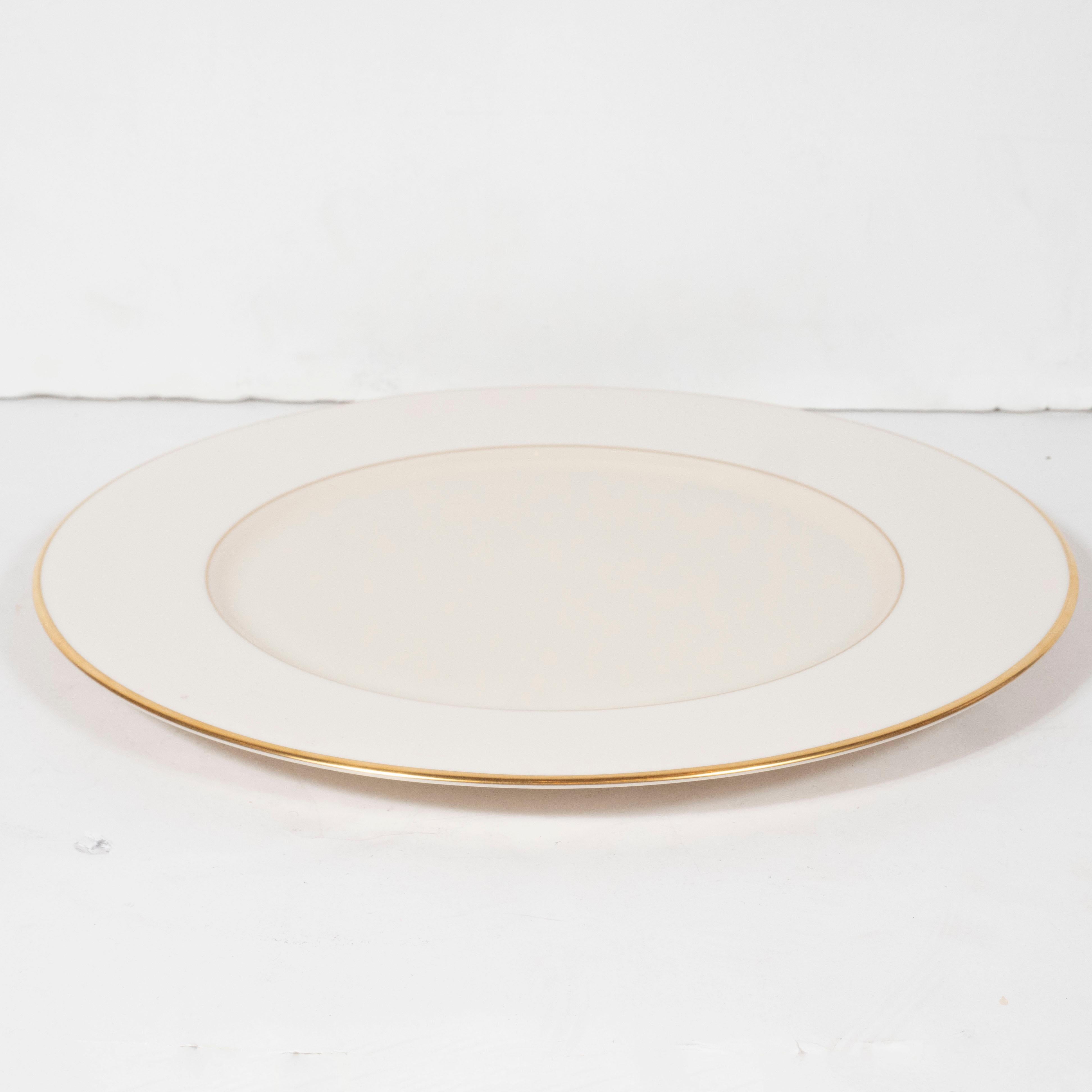 This elegant set of six charger plates were realized by the esteemed maker Lenox in the United States. They feature 24-karat gold banding in the center, as well as along the outer perimeter on a bone china background. With their clean modernist