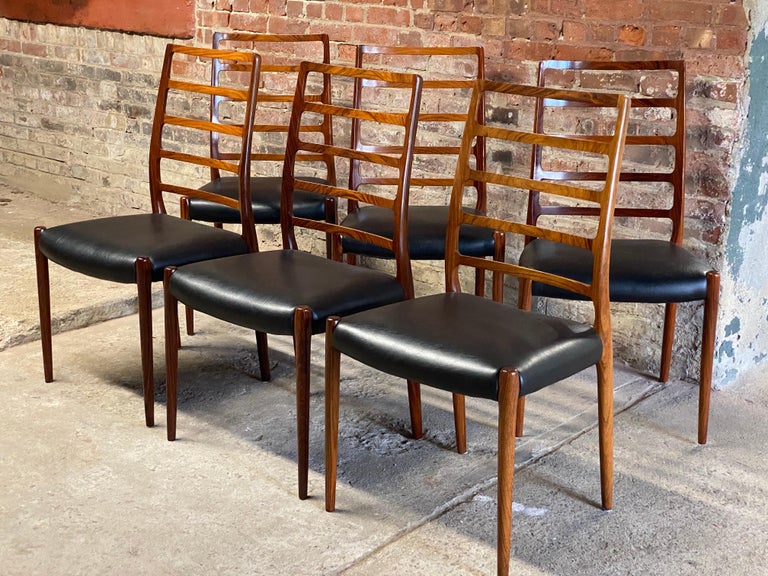 Set of six impressive Model 82 ladder back chairs by Niels O. Moller for J.L. Moller Mobelfabrik. Featuring solid Rosewood construction with newly recovered black vinyl seats, elegantly tapered legs, and comfortable ladder backs. Circa 1960-70. All