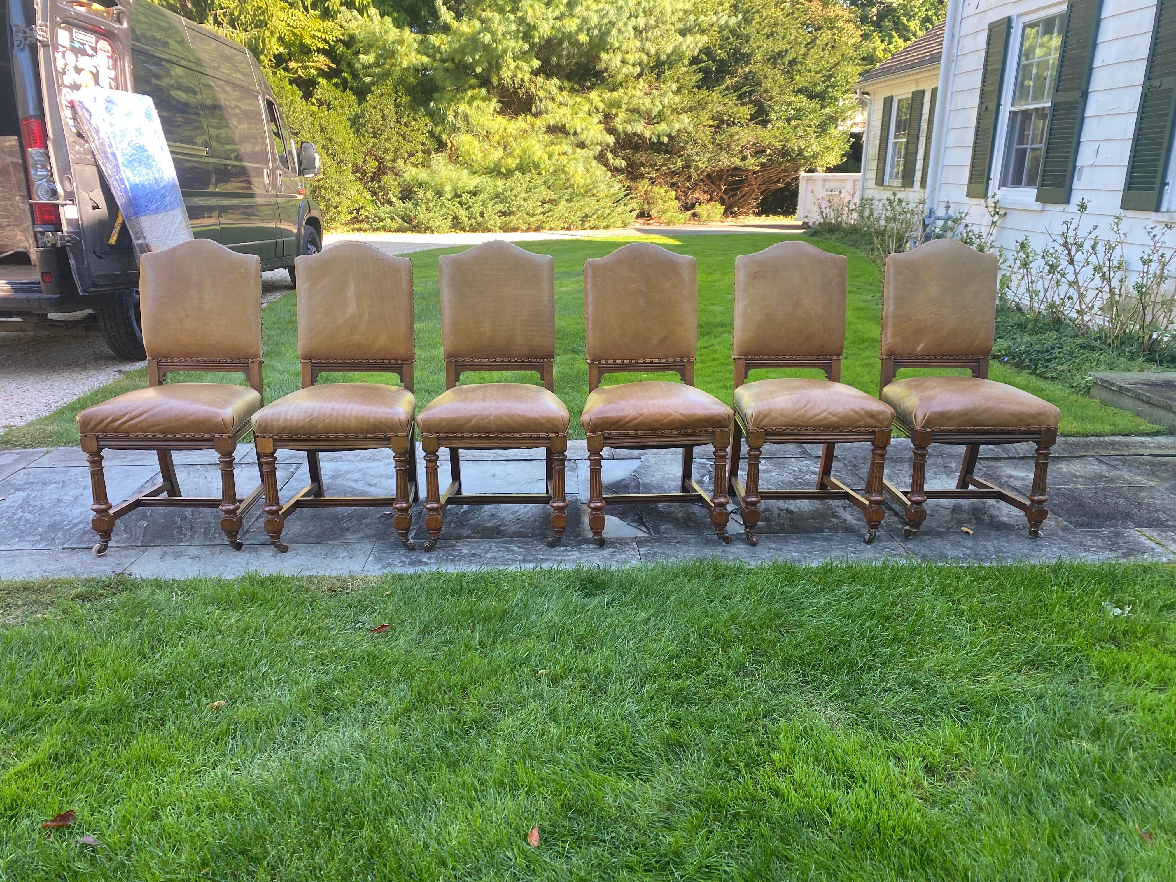 Set of Six Antique Oak Dining Chairs with Leather Upholstery, 20th Century.
This set of antique dining chairs features a sturdy oak frame with turned and fluted legs. The seats and backs are upholstered in a warm, caramel leather, secured with brass