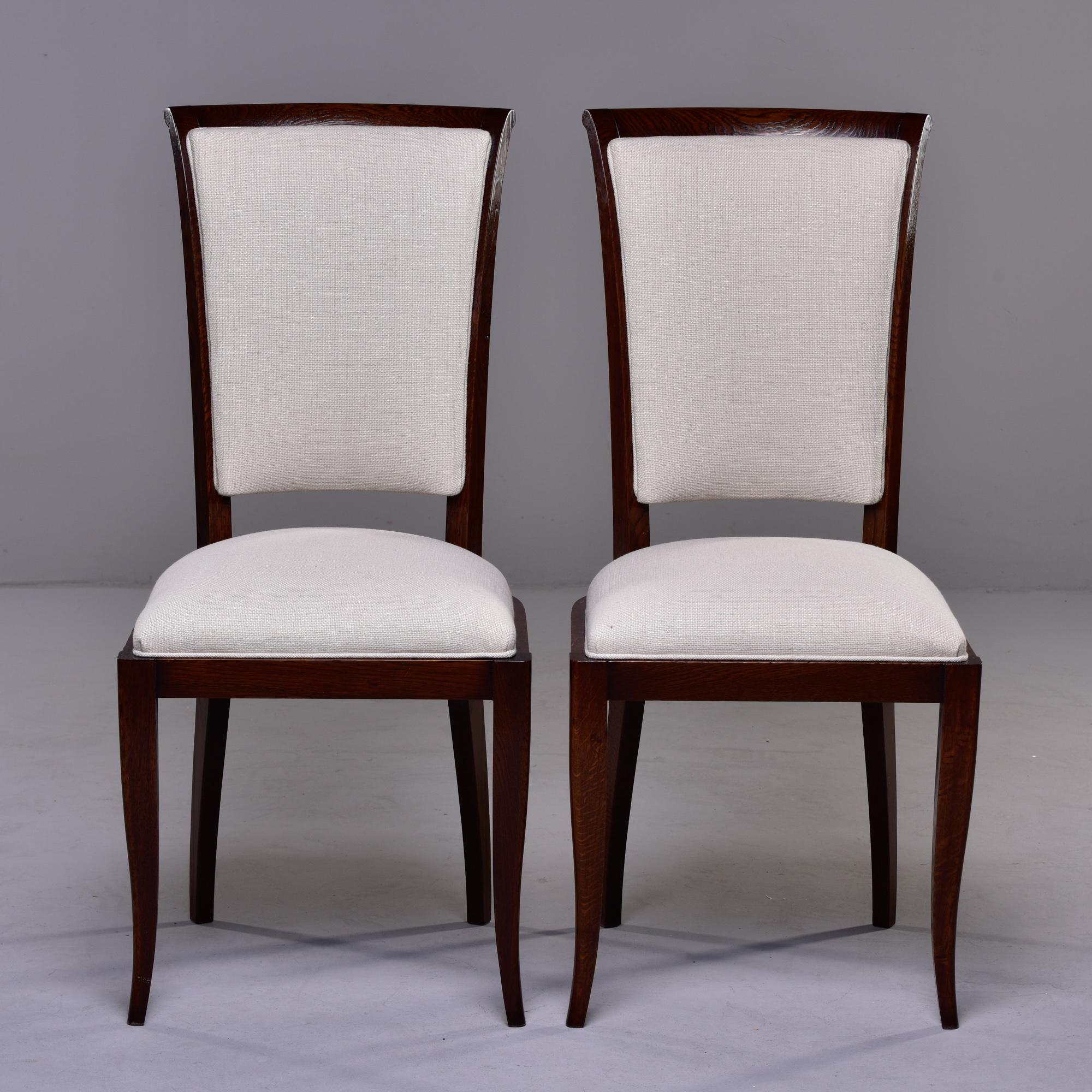 Circa 1950s set of French oak dining chairs with sleek profile, dark stain and upholstered seats and backs. Fabric is off-white linen blend dobby weave. Unknown maker. Sold and priced as a set of six. 

Measures: Seat height: 20” 
Seat width: