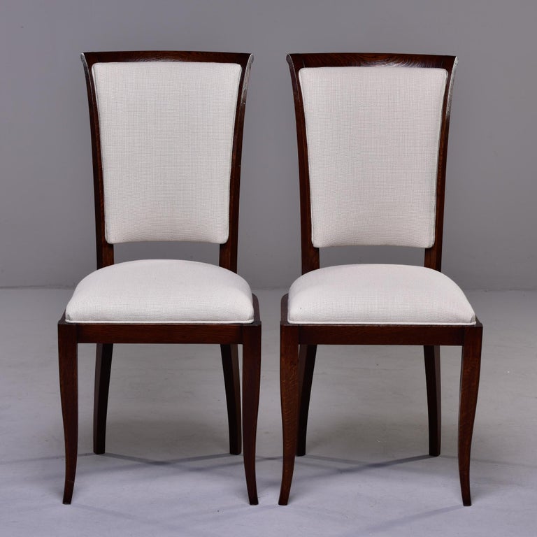Circa 1950s set of French oak dining chairs with sleek profile, dark stain and upholstered seats and backs. Fabric is off-white linen blend dobby weave. Unknown maker. Sold and priced as a set of six. 

Measures: Seat height: 20” 
Seat width: