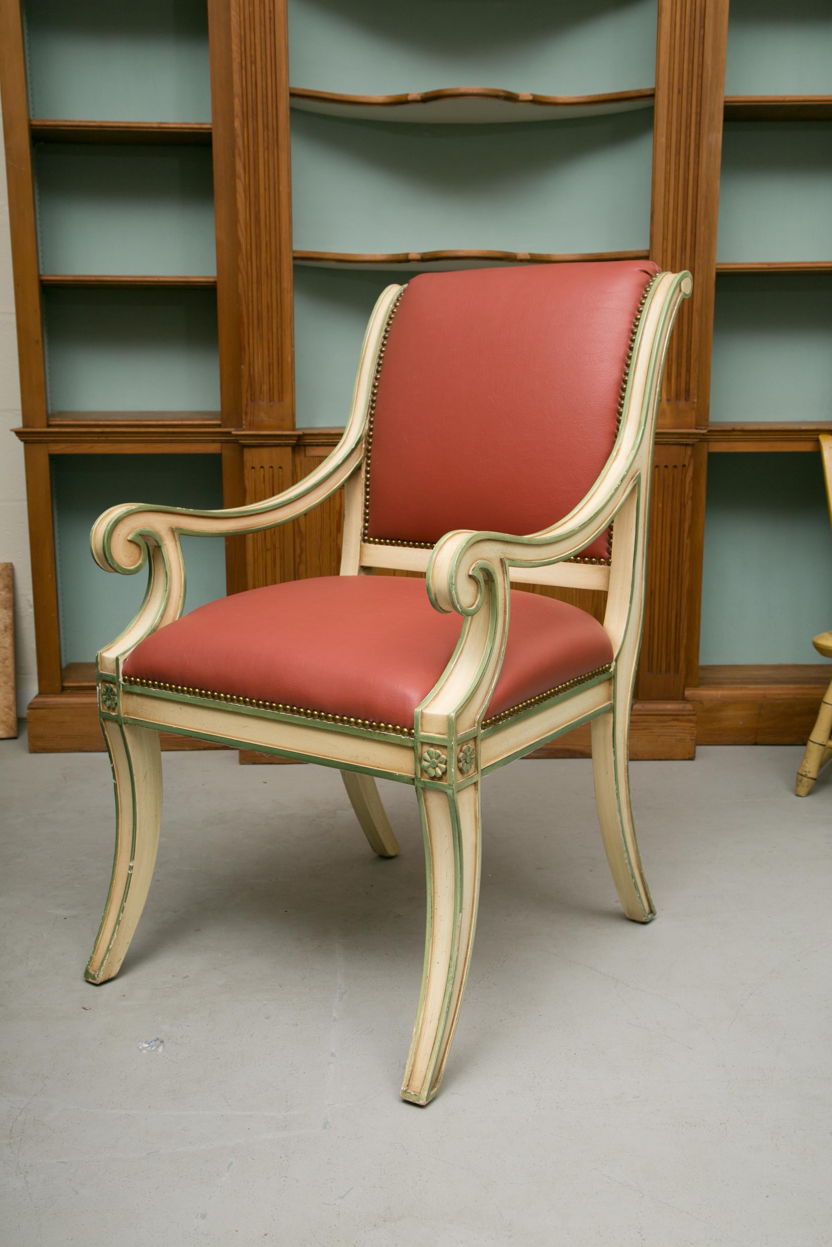 This is a decorative set of six cream-painted Regency style dining arm chairs highlighted with green. All chairs have both fully upholstered back and seats in coral leather. The frames consist of out-scrolling arms and klismos style legs, circa 20th