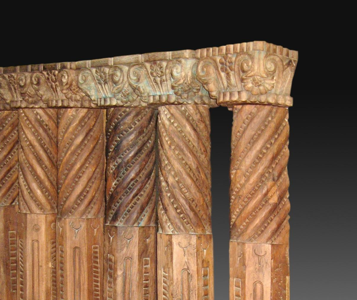 Row of six carved wooden pillars that have capitals in the upper part and stone bases carved in the lower end (these are grouped in pairs). The shafts have three different sections (square, polygonal and spiral) and a decoration in relief along