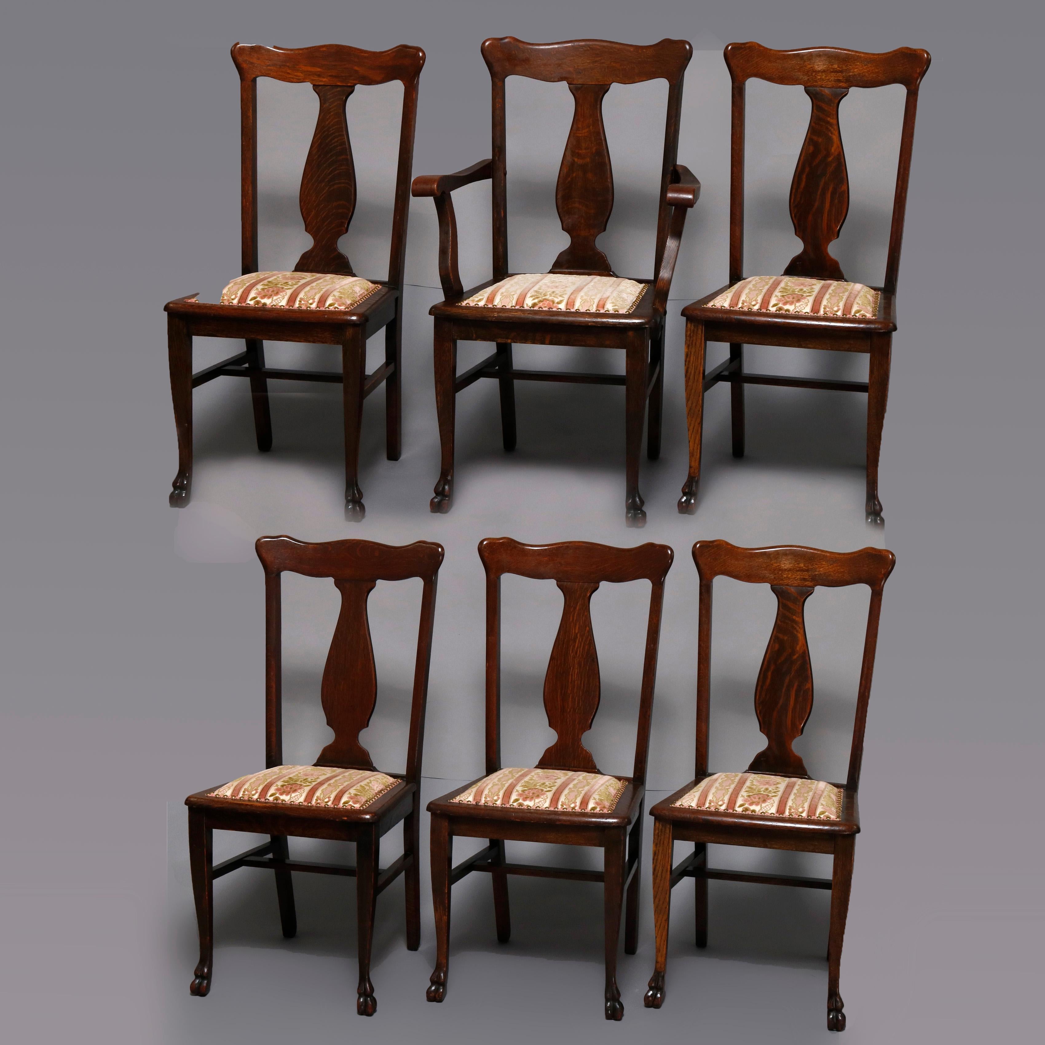 A set of 6 dining room chairs by R. J. Horner offer oak construction and includes one armchair and five side chairs with T-back urn form slats surmounting upholstered seats and raised on legs terminating in carved stylized pay feet, circa