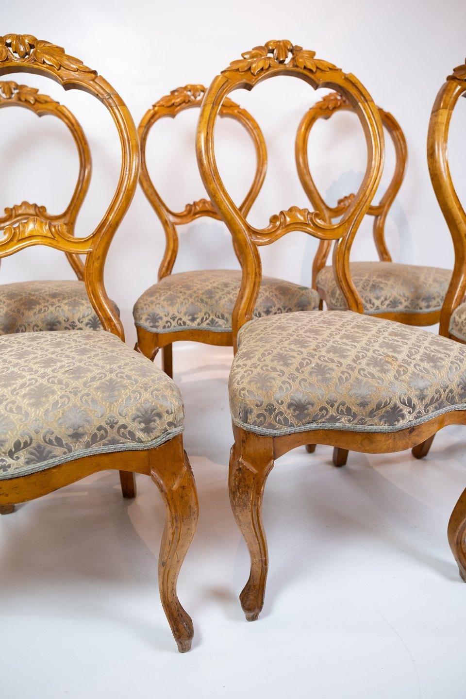 Das Set aus sechs Rokoko-Esszimmerstühlen aus hellem Mahagoni und mit aufwändig gemustertem Stoff verziert, erinnert an die Opulenz und Eleganz der 1760er Jahre. Diese Stühle sind exquisite Beispiele des Rokoko-Stils, der sich durch aufwändige