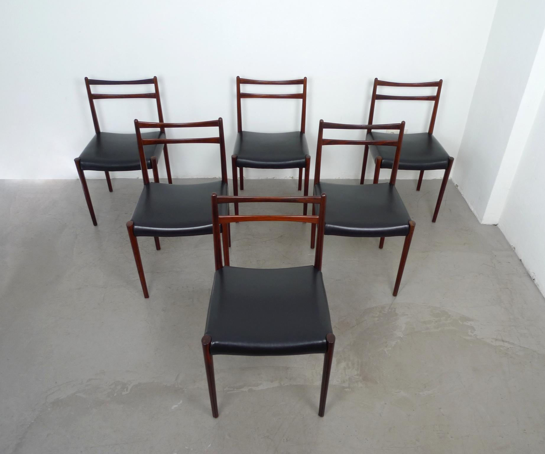 This set of six dining chairs was produced in Denmark in the 1960s. The graceful frames are made of rosewood and the seats are covered with black leatherette. The chairs are in good original condition, but the seats show small scratches.