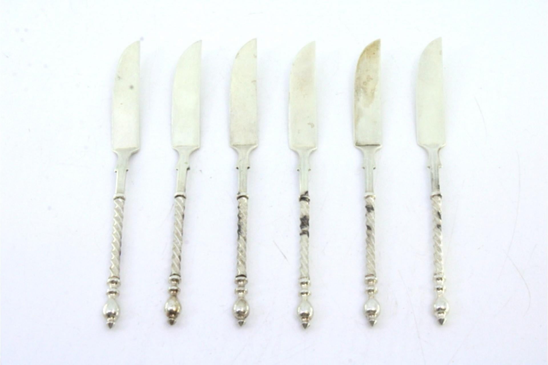 Description: Set of six silver butter knives with twisted handles and applications at the ends. Metal: Silver. Origin: Portuguese. Brand: Cabeça de escravo. Weight: 57.99 grams. Dimensions: 12cmx1.1cm. Content: 833/1000. Assay Mark: Yes, between