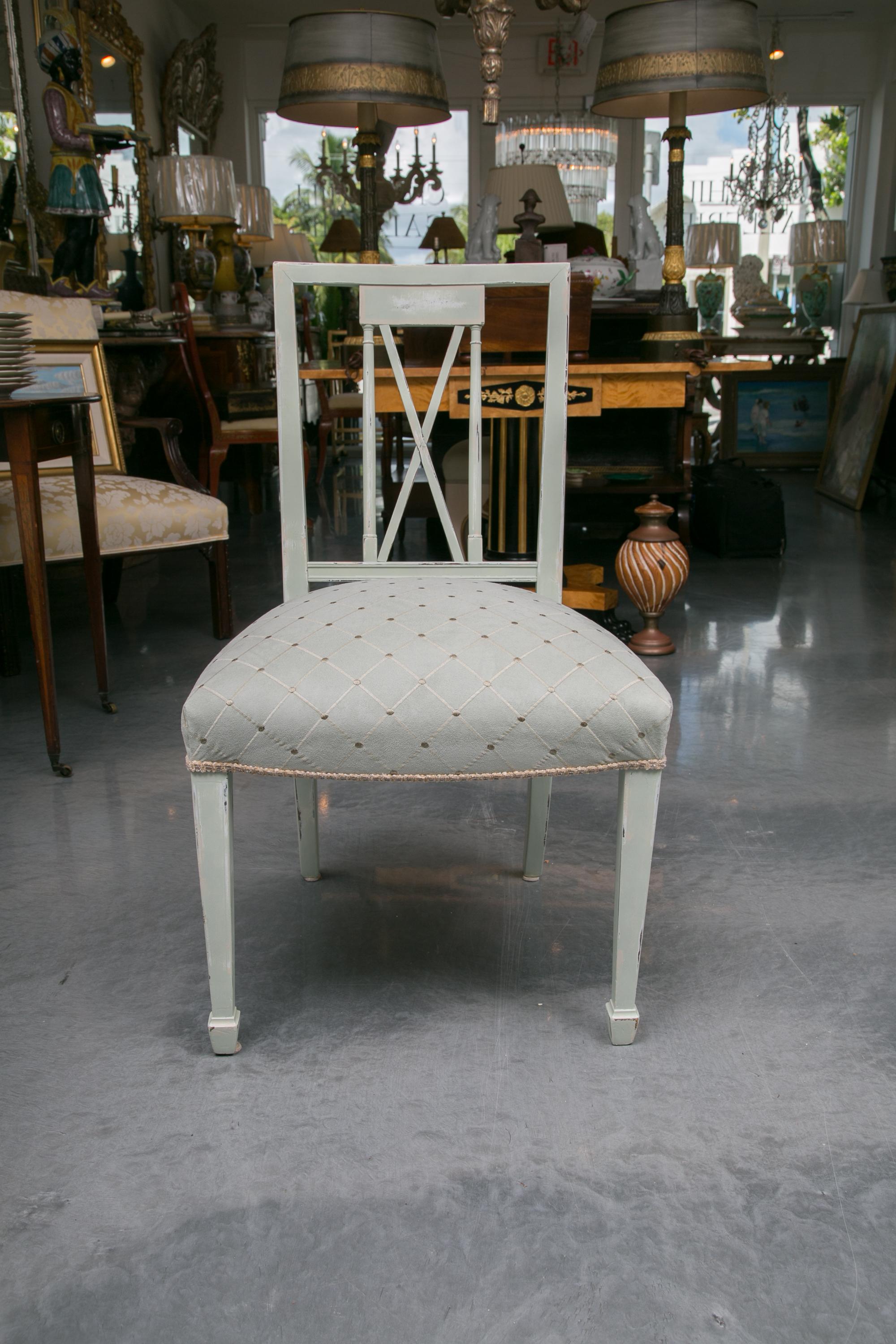 This set of six dining chairs painted in a soft blue pastel, consisting of two arm and four side chairs. The chairs have a straight back rail over a cross-hatch back spat and upholstered in a suede fabric. The fully padded seat is supported on the