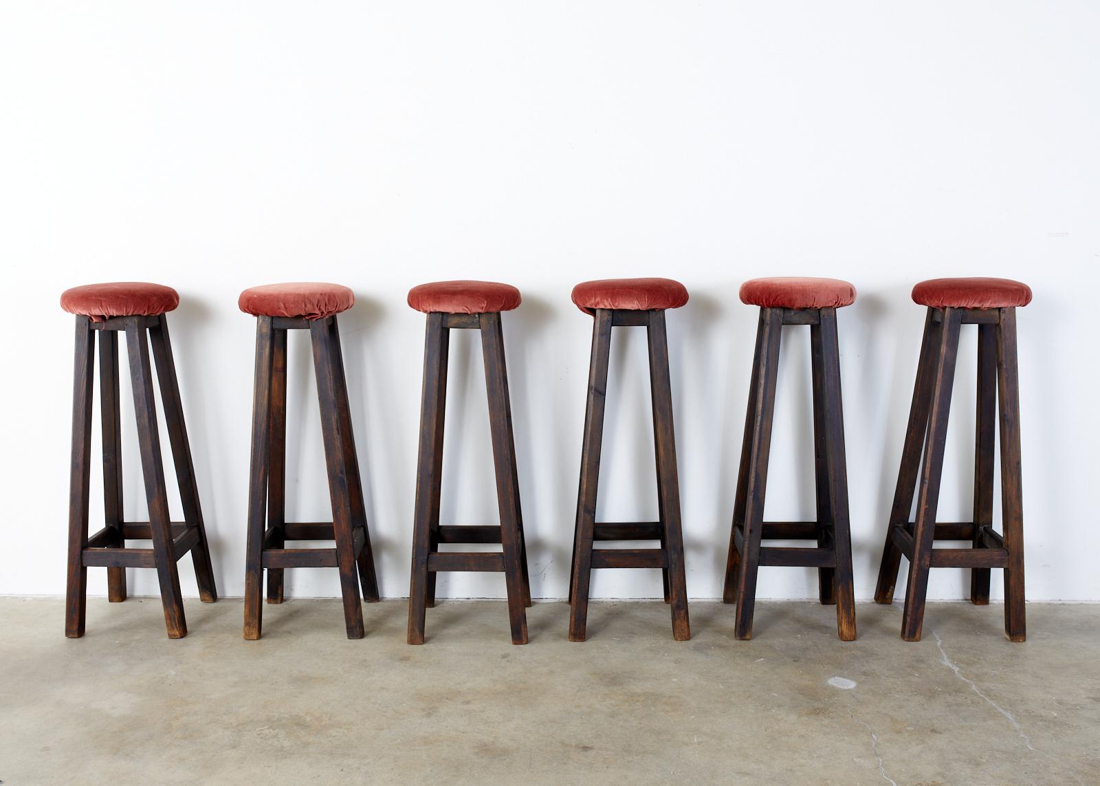 Rustic set of six matching pub style barstools featuring tall, narrow frames, crafted from oak with chambered legs conjoined by stretchers. Dark finish on the oak has an aged, faded patina. Topped with velvet covered seat cushions that would benefit