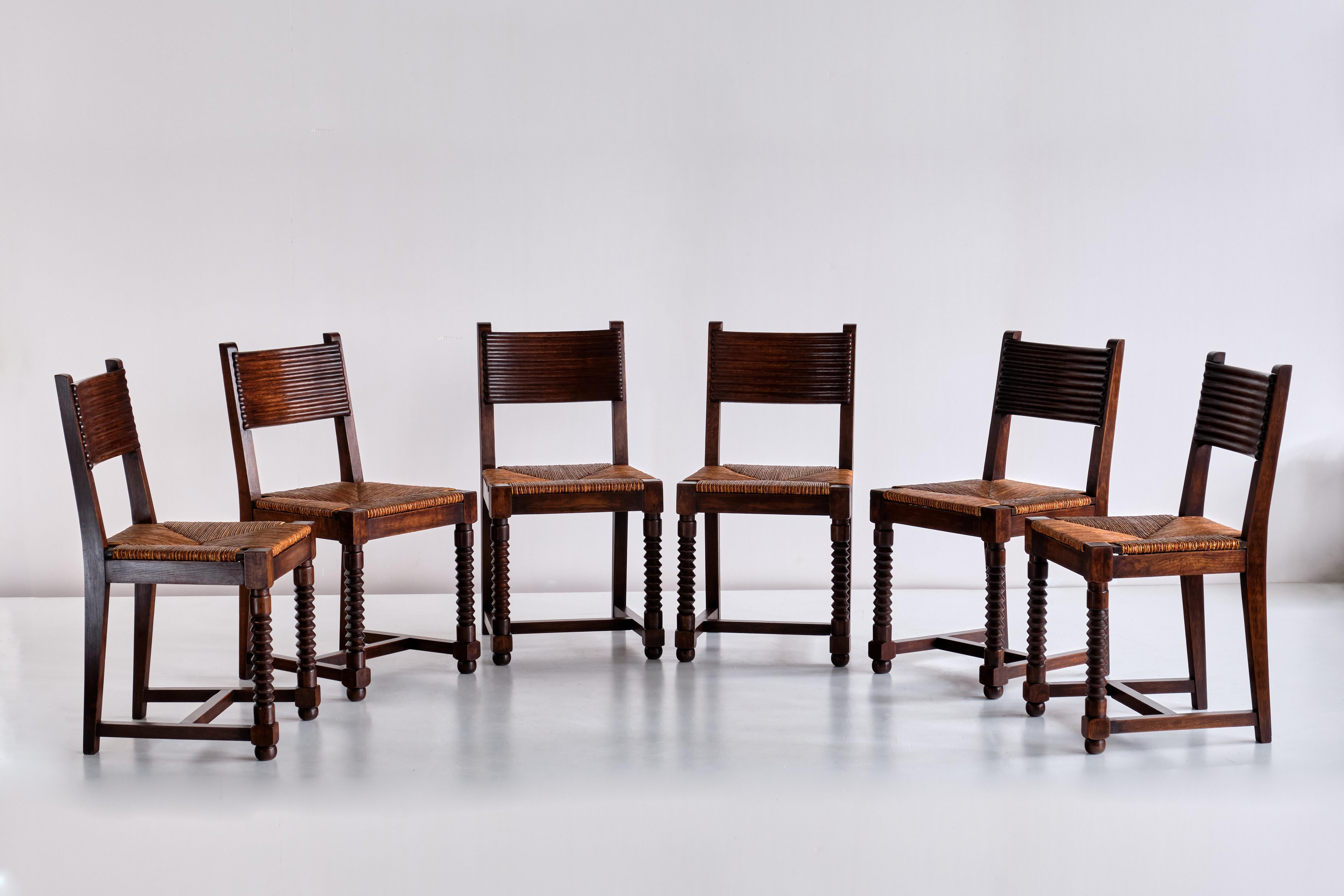 This striking set of six dining chairs was designed by Victor Courtray and produced in the Northern Basque region around the city of Biarritz in the 1940s. 
The chairs are in solid, stained oak with the seat in woven rush. The carved disc shape of