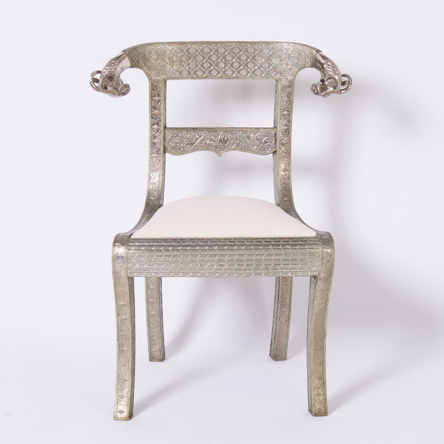 Rare and remarkable set of six vintage Anglo Indian side chairs crafted in indigenous hardwood clad in metal, decorated with hammered and pressed floral and geometric motifs, featuring nickel plated ram's heads on the crests and sabre front legs.