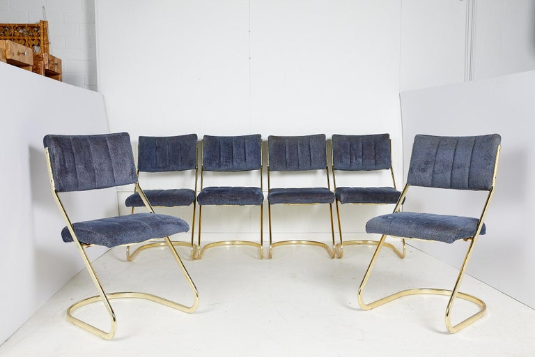 American midcentury set of six brass cantilever dining chairs by Douglas Furniture Corporation. The tubular brass frame is in the style of Milo Baughman and supports a channel upholstered seat and back in blue fabric, circa 1970s.