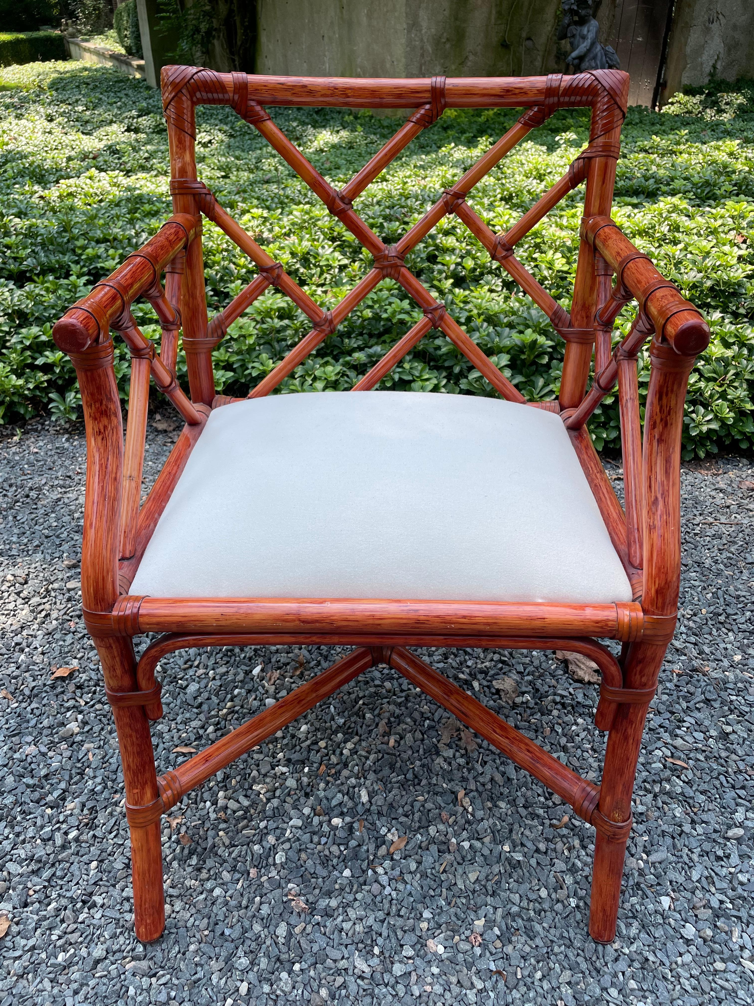 A glamorous classic set of six Chinese Chippendale French rattan chairs with cushioned seats. There are four side chairs and two open arm chairs. The rattan is in excellent condition and has a wonderful toffee colored patina. The upholstered seats