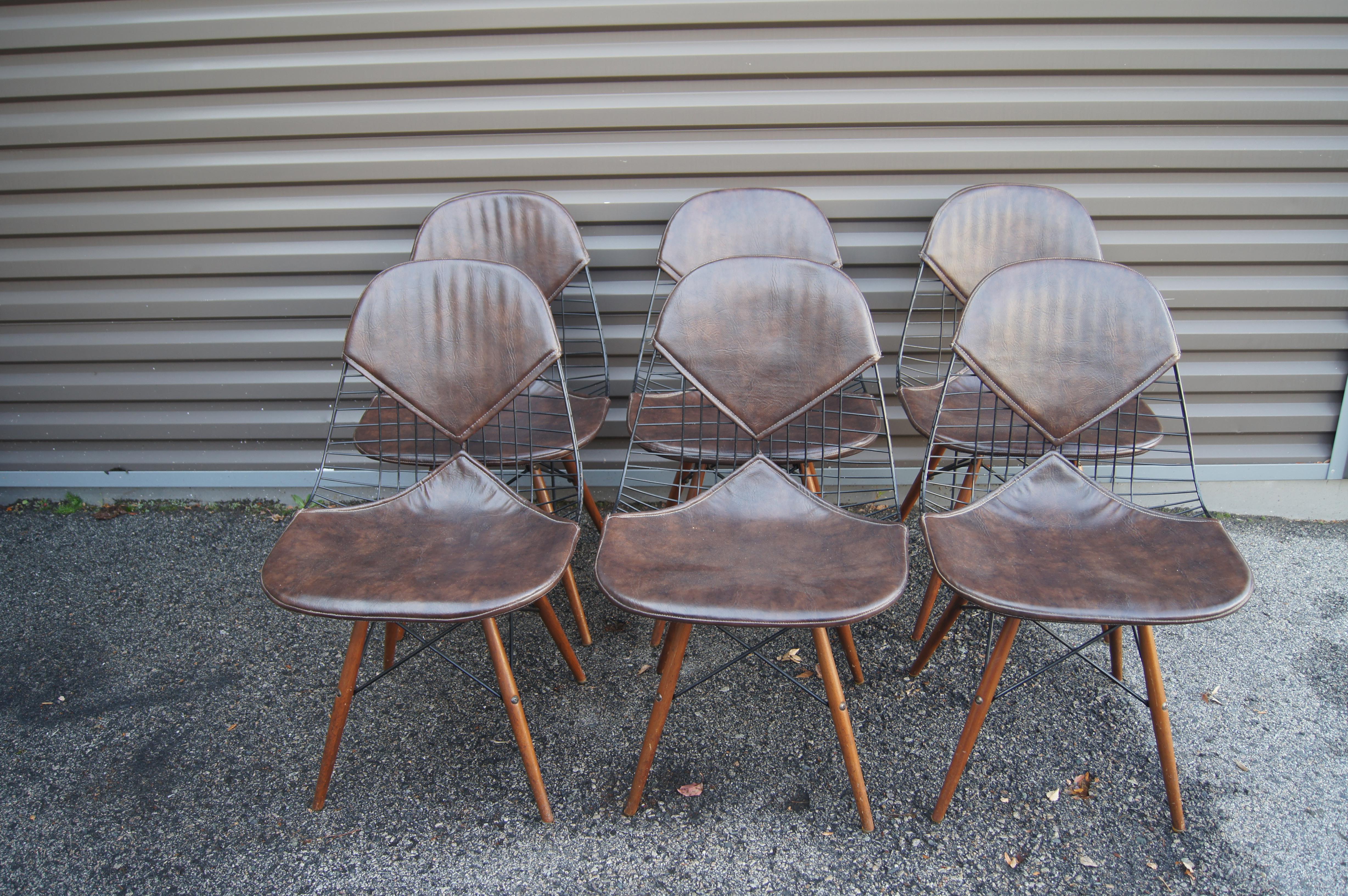 Charles and Ray Eames designed their classic wire dining chairs for Herman Miller in 1951. This early set of six chairs features black powder-coated wire frames on wooden dowel legs with brown leather 