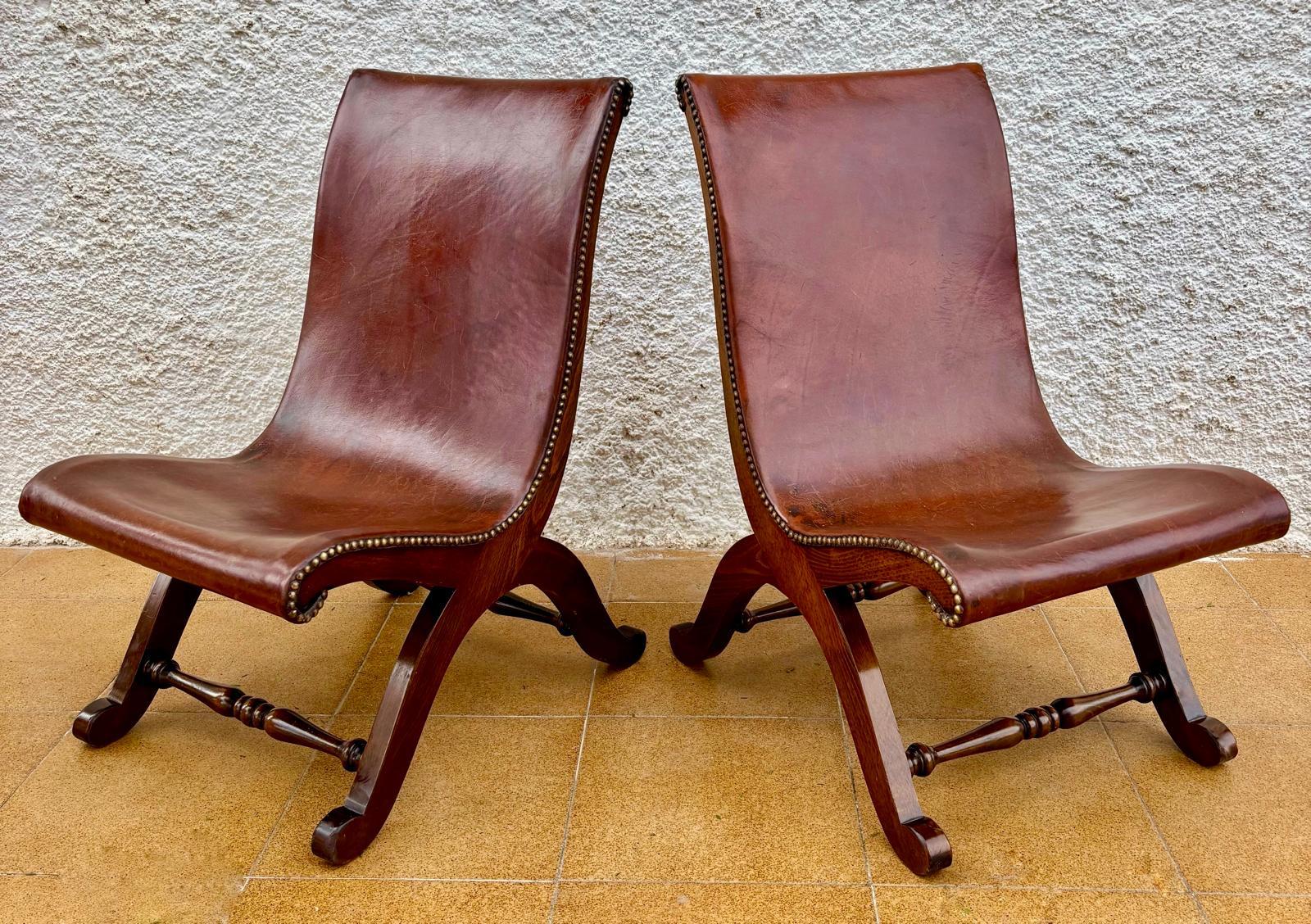 Coppia di sedie spagnole disegnate da Pierre Lottier per Valenti, anni Cinquanta. Struttura in legno di Oak dalle linee curve e armoniose su cui poggia lo schienale in pelle marrone con borchie in metallo. Questa sedia divenne molto popolare in