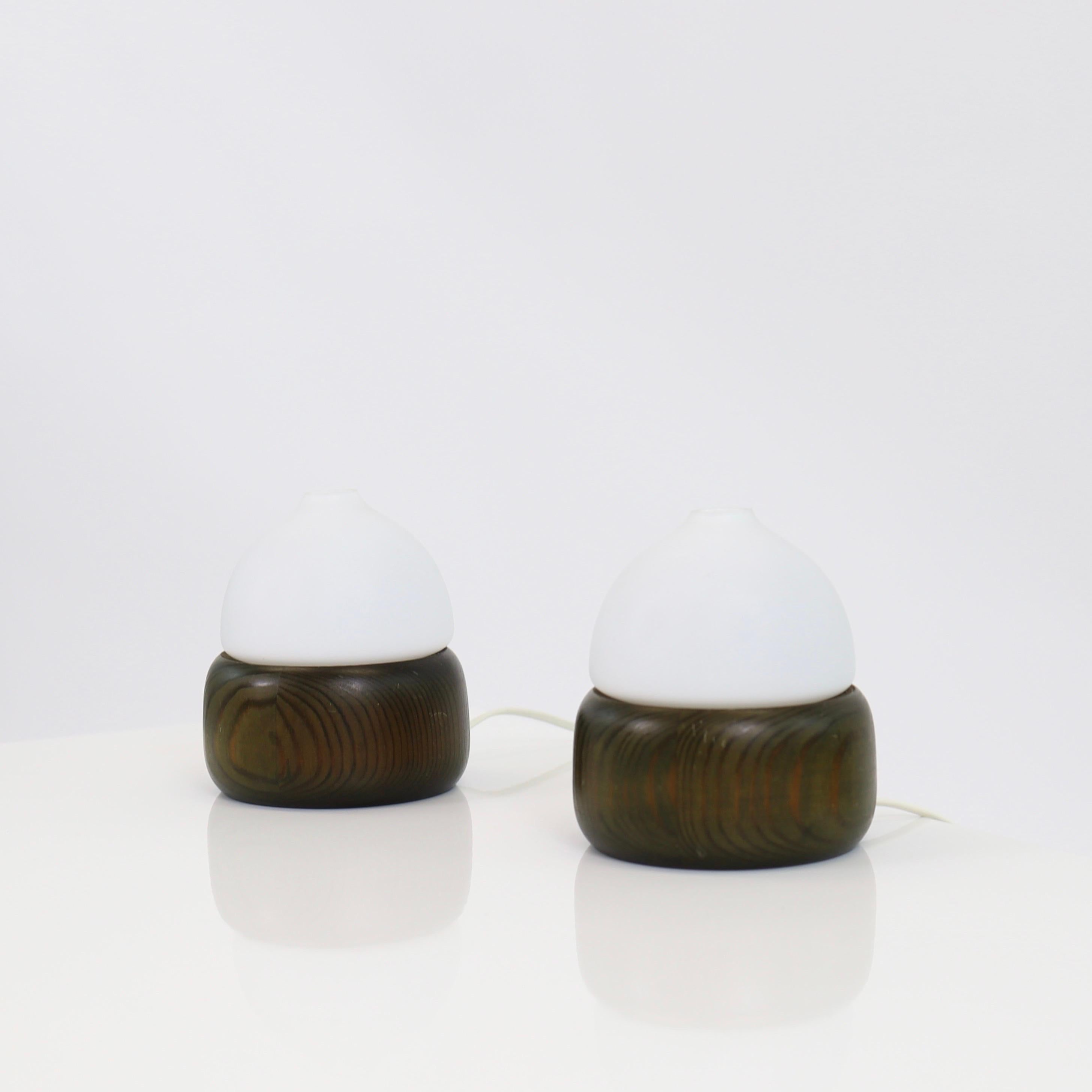 Set dark stained Pine Wood night lamps with white glass shades made by Aneta in the 1970s. A soft Scandinavian touch.

* A set of desk lamps / night lamps in dark stained pine wood with white round glass shades
* Manufacturer: Aneta, Sweden
* Year: