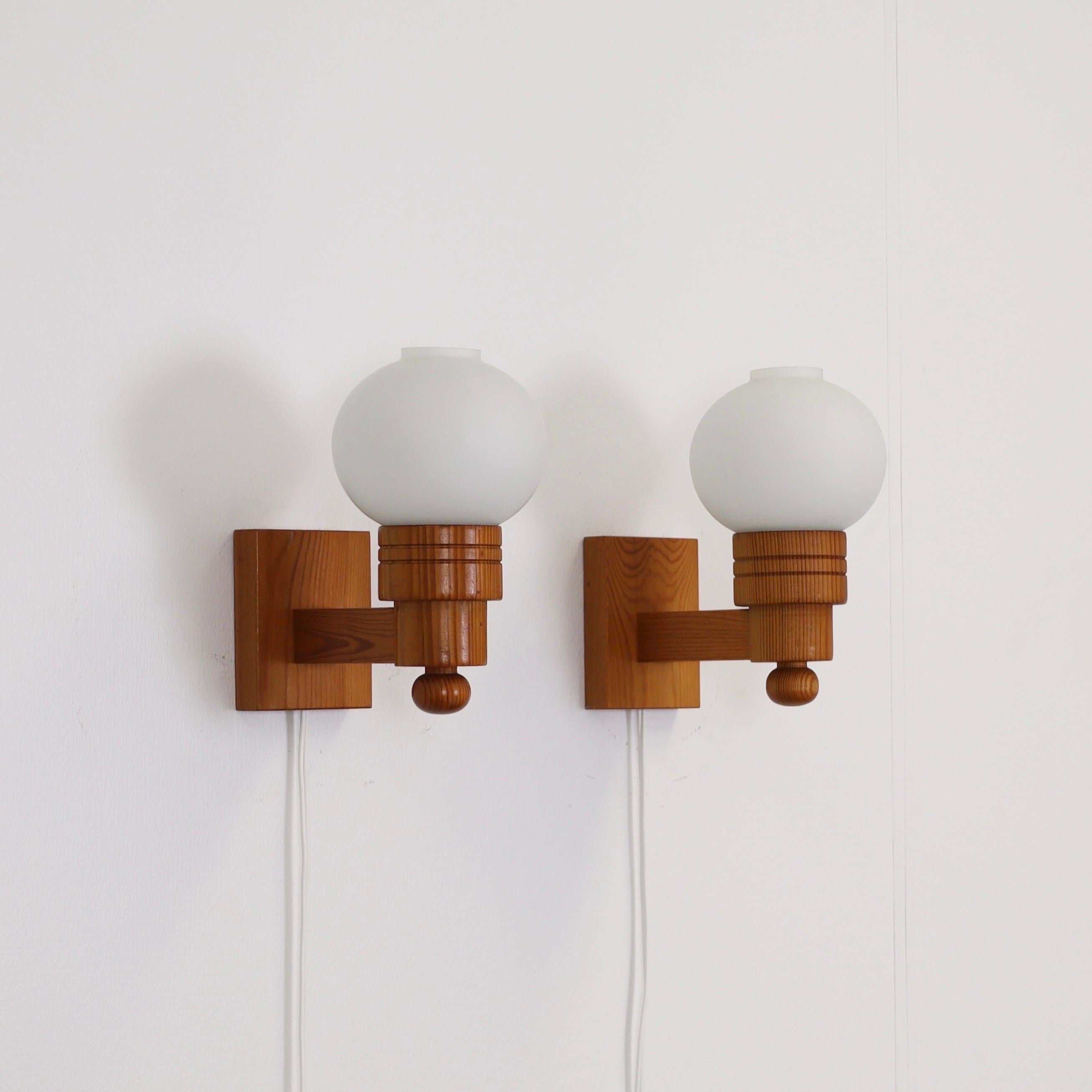 A set Swedish Modern Pine wood Wall lamps with white glass shades made by Aneta in the 1970s. The set is a fine Scandinavian addition to a beautiful place. 

* A pair (2) of wall lamps in Pine wood with white round glass shades
* Manufacturer: