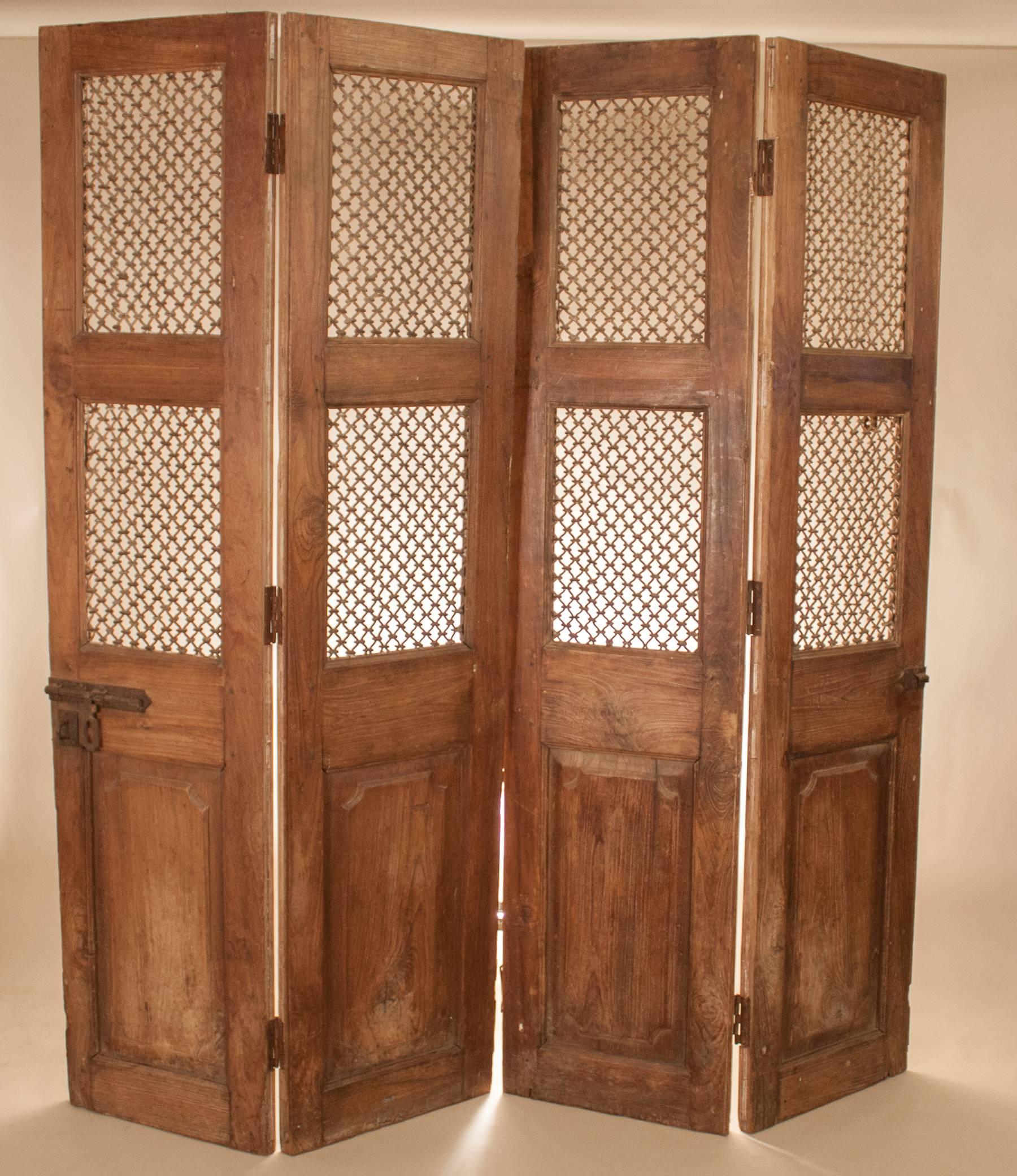 A set of teak wood doors, circa 1900, with woven iron grilles and slide locks from Gujarat, India. The set is comprised of two pairs of doors, each with two pegged joint panels hinged together, for a total of four panels. Originally used as a front