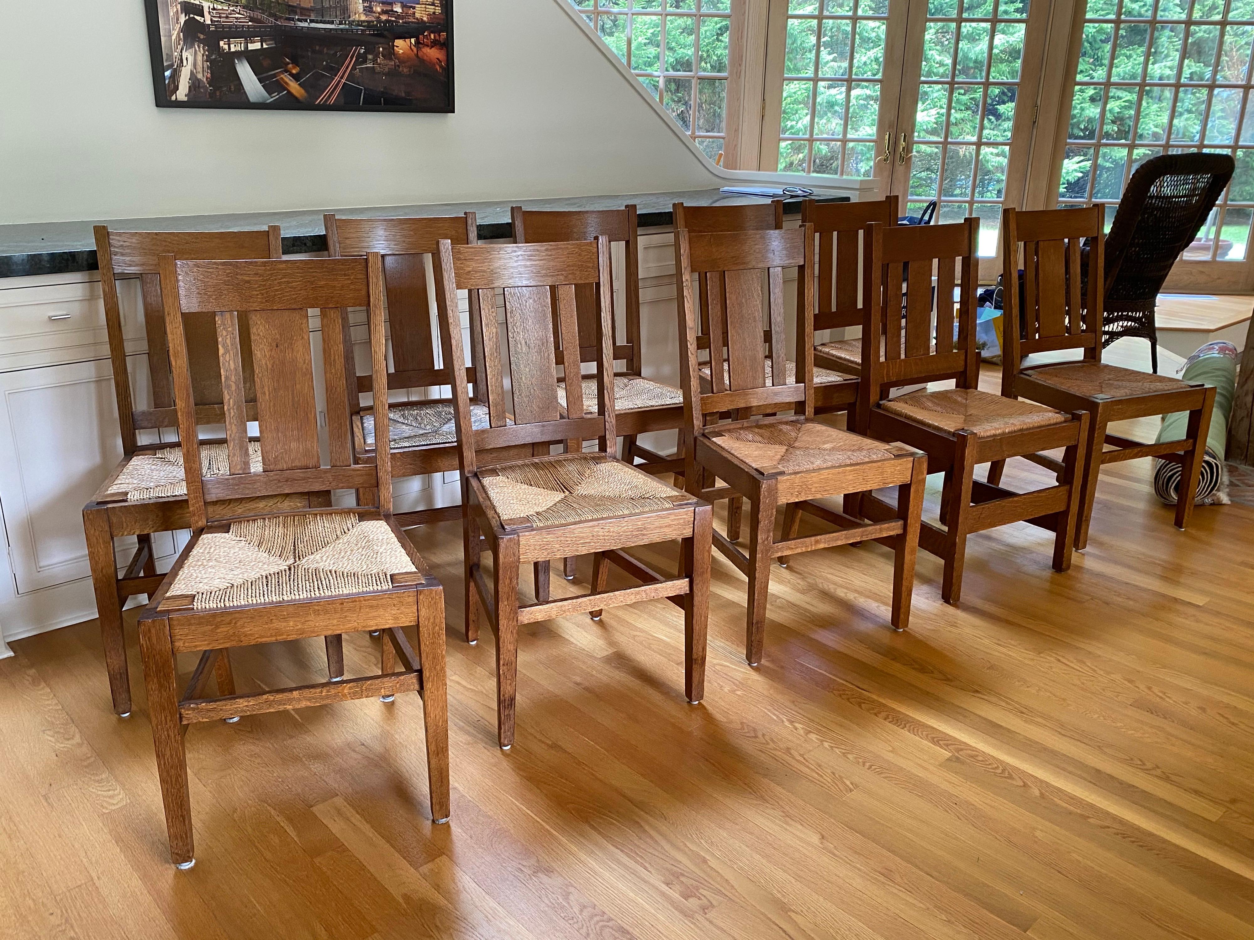Set of ten Arts & Crafts Stickley-style oak dining chairs. A matched set of eight + two additional. All with rush seating. Two of the chairs look to be added to the set and go well but are not original. The front leg posts of the two chairs project
