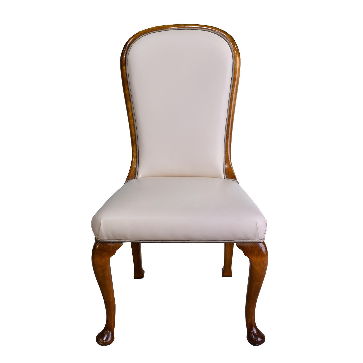 A handsome set of ten (10) dining chairs that comprise two (2) armchairs and eight (8) side chairs with birchwood frames, with high rounded backs and cabriole legs with pad feet. Side chairs are upholstered in a cream-colored leather or faux