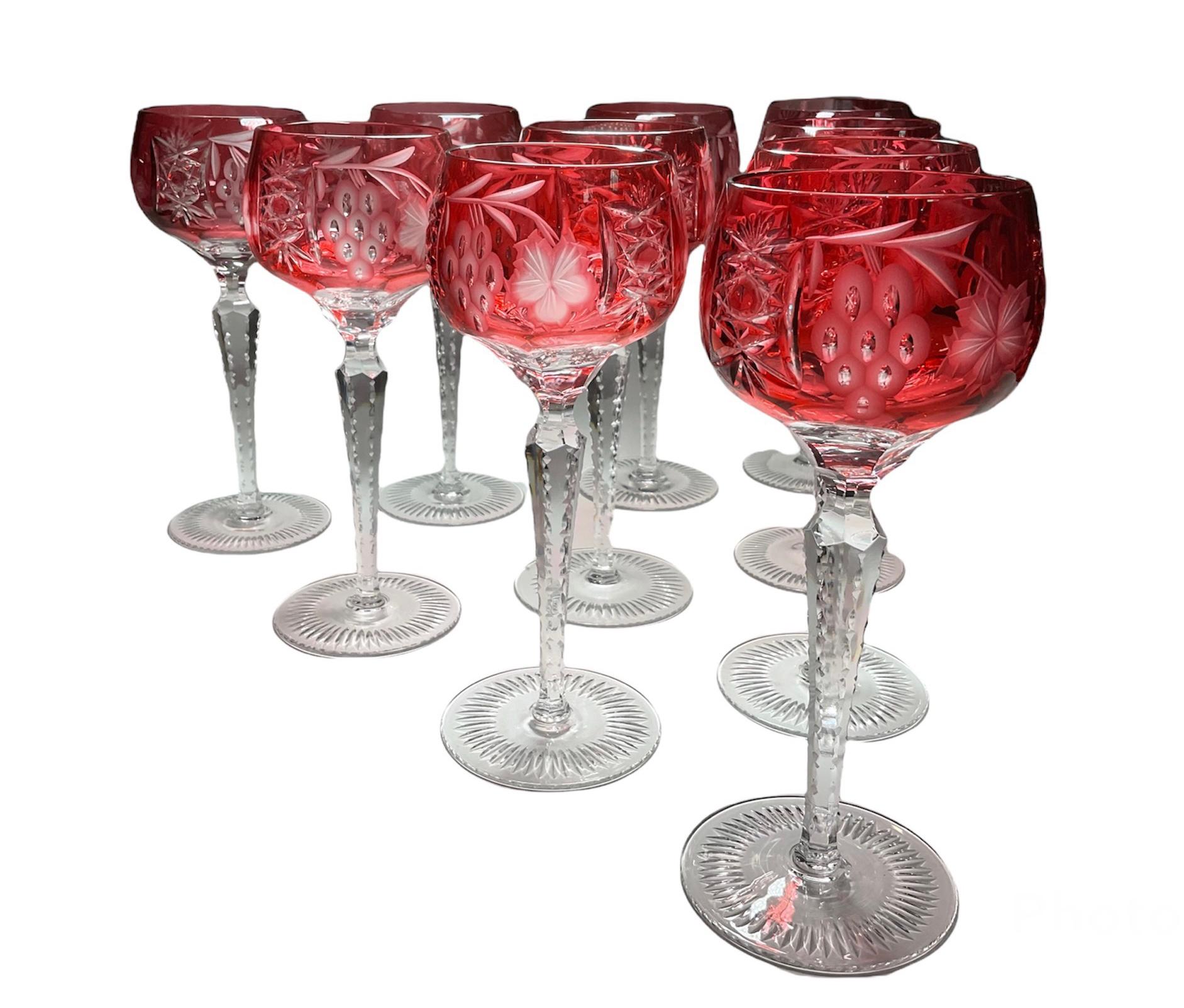 This is a set of ten cranberry color to clear wine cut crystal glasses. Their round bowls are decorated with etched frosted grapevine branches and clear grapes bunches alternated by cut crystal patterns of fans and hobstars. Below the bowls, there