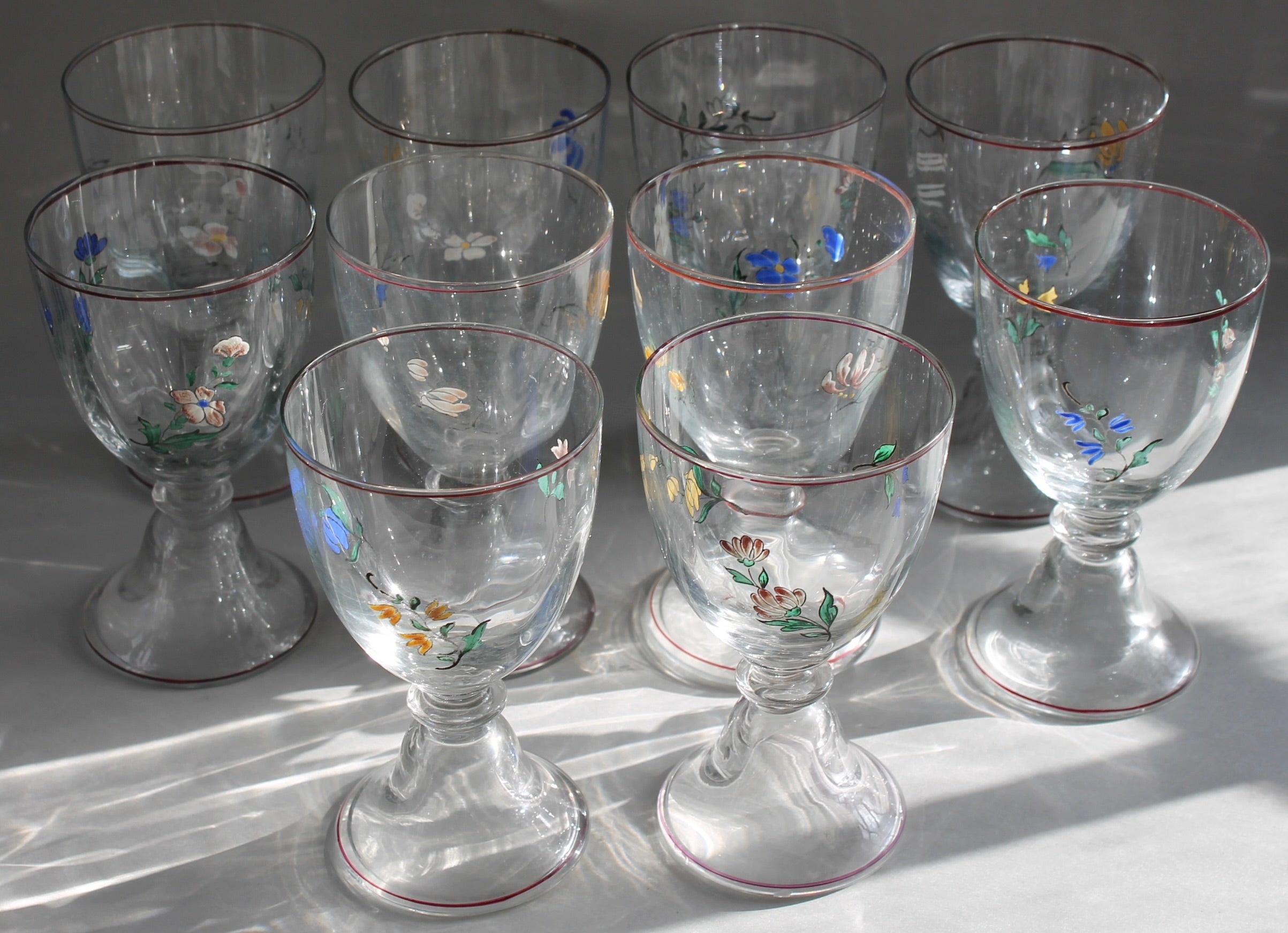 Dieci bicchieri da acqua in cristallo dipinti a mano.  Smalto multicolore
ciuffi di foglie e fiori in un leggero stile 