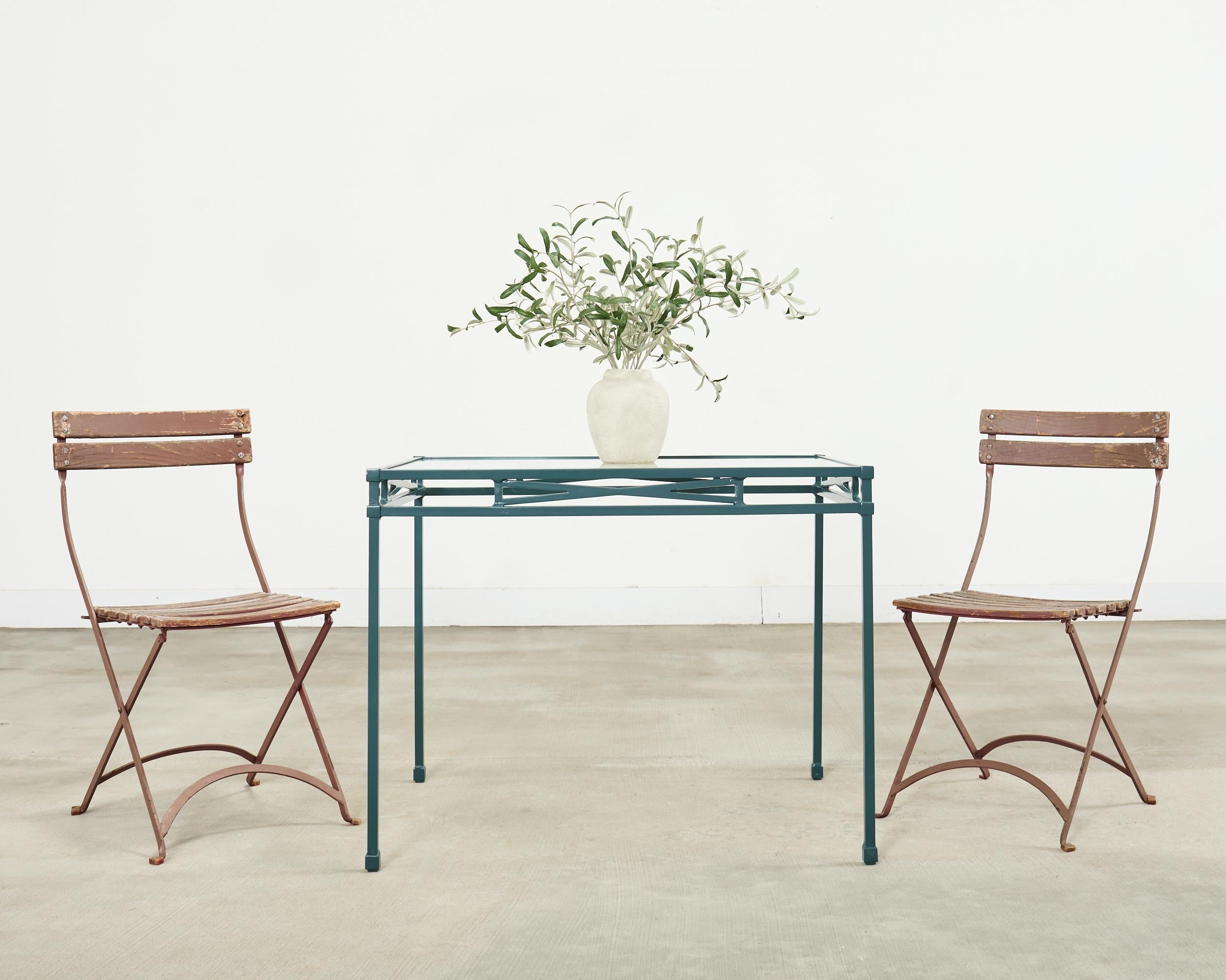 Weathered set of ten mid-century modern cafe/bistro dining chairs perfect for the patio or garden. The chairs feature a patinated iron frame with wood slats on the back and seat. The chair frames fold and are crafted from thin flat iron with
