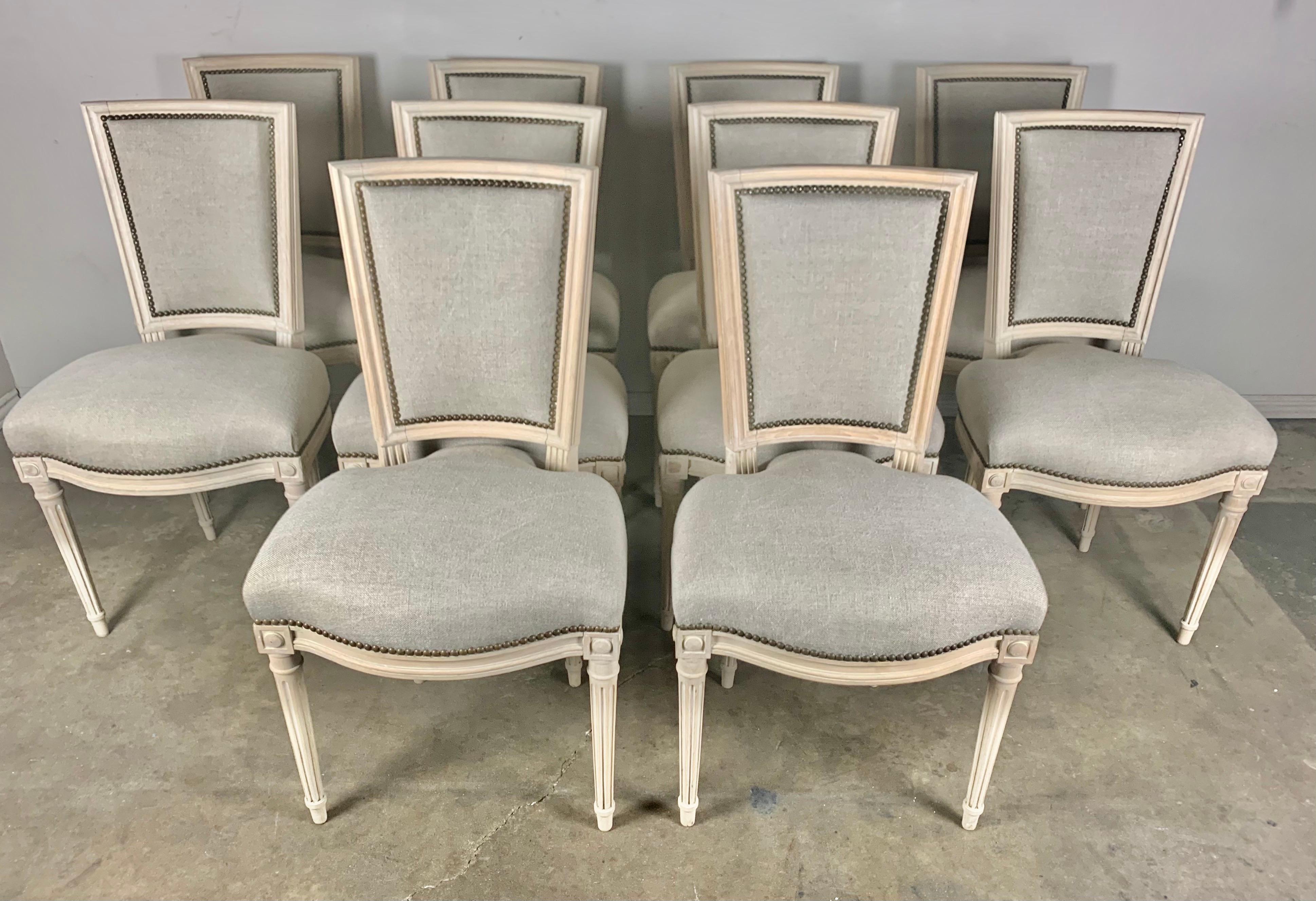 Set of ten French Louis XVI Style dining chairs standing on four straight fluted legs that have clean simple lines for your elegant space. The natural colored wood frames are newly upholstered in a washed Belgium linen with antique brass nailhead
