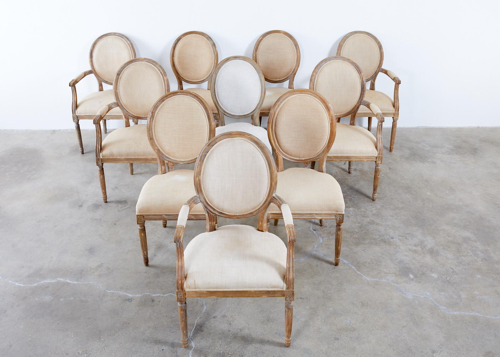 Large set of ten weathered oak dining chairs made in the neoclassical French Louis XVI taste. The set consists of five generous armchairs and five matching side chairs measuring 20 inches wide. The chairs feature a Belgian linen upholstery with an