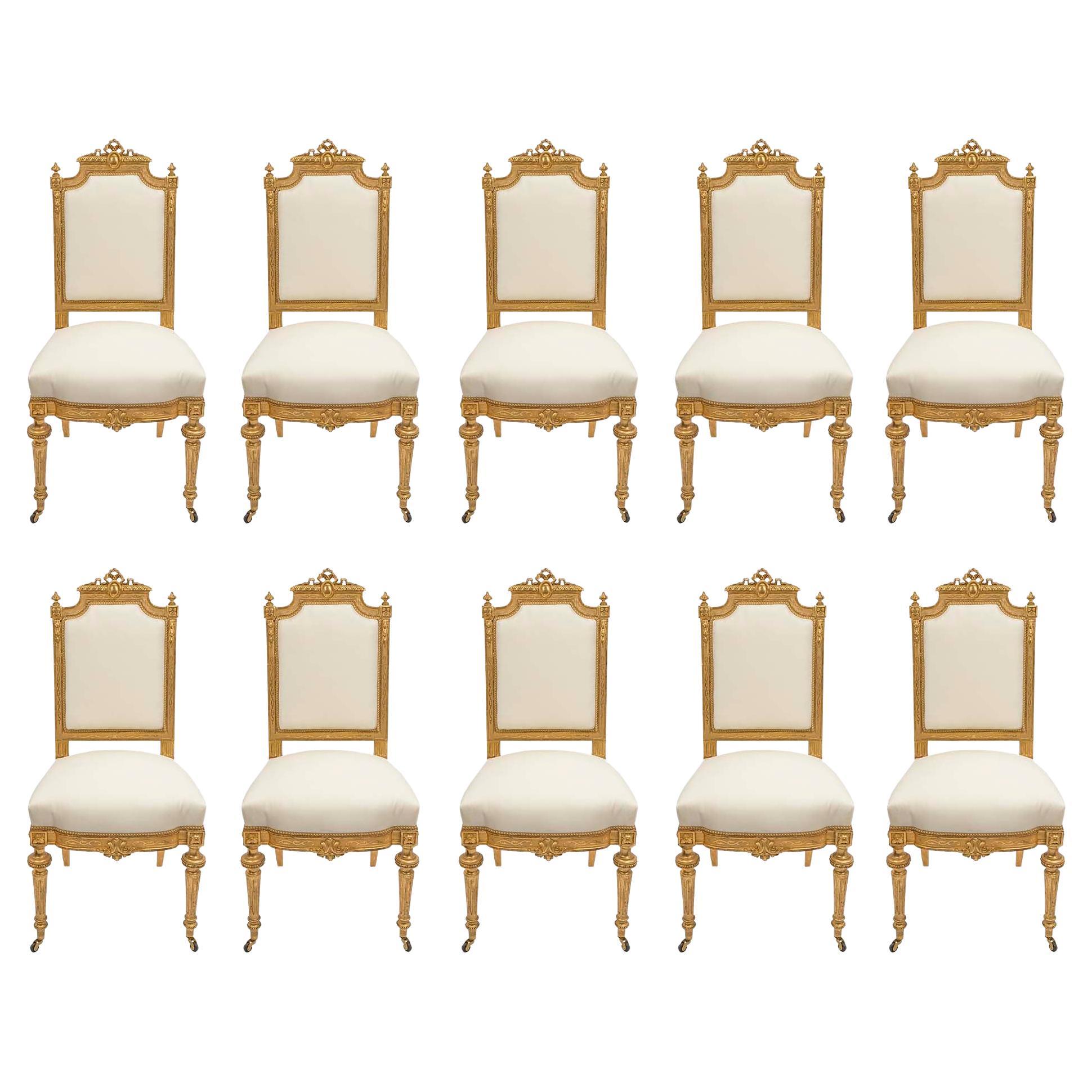 An elegant and high quality set of ten French mid 19th century Louis XVI st. Giltwood dining chairs. Each chair is raised by two finely carved circular fluted tapered front legs, with the original casters and block rosettes above, and two lightly