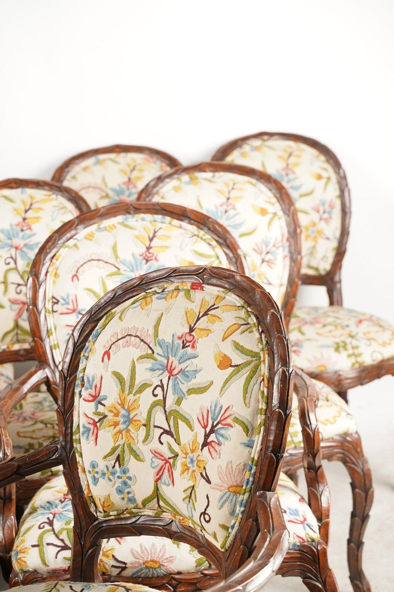 Set of Ten chairs hand carved in a leaf pattern and upholstered in floral crewelwork. This set consists of two armchairs (26 1/4 inches wide; 26 inches deep; 39 1/2 inches high; seat height: 19 inches) and eight side chairs (21 1/4 inches wide; 25