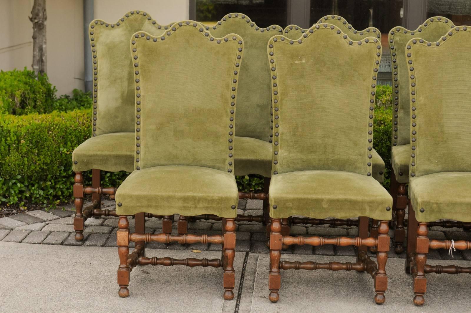 A set of ten Italian Baroque style dining room side chairs from the early 20th century with camelbacks, turned legs, green upholstery and nailheads. Each of this set of Italian side chairs features a slightly slanted green upholstered camelback,