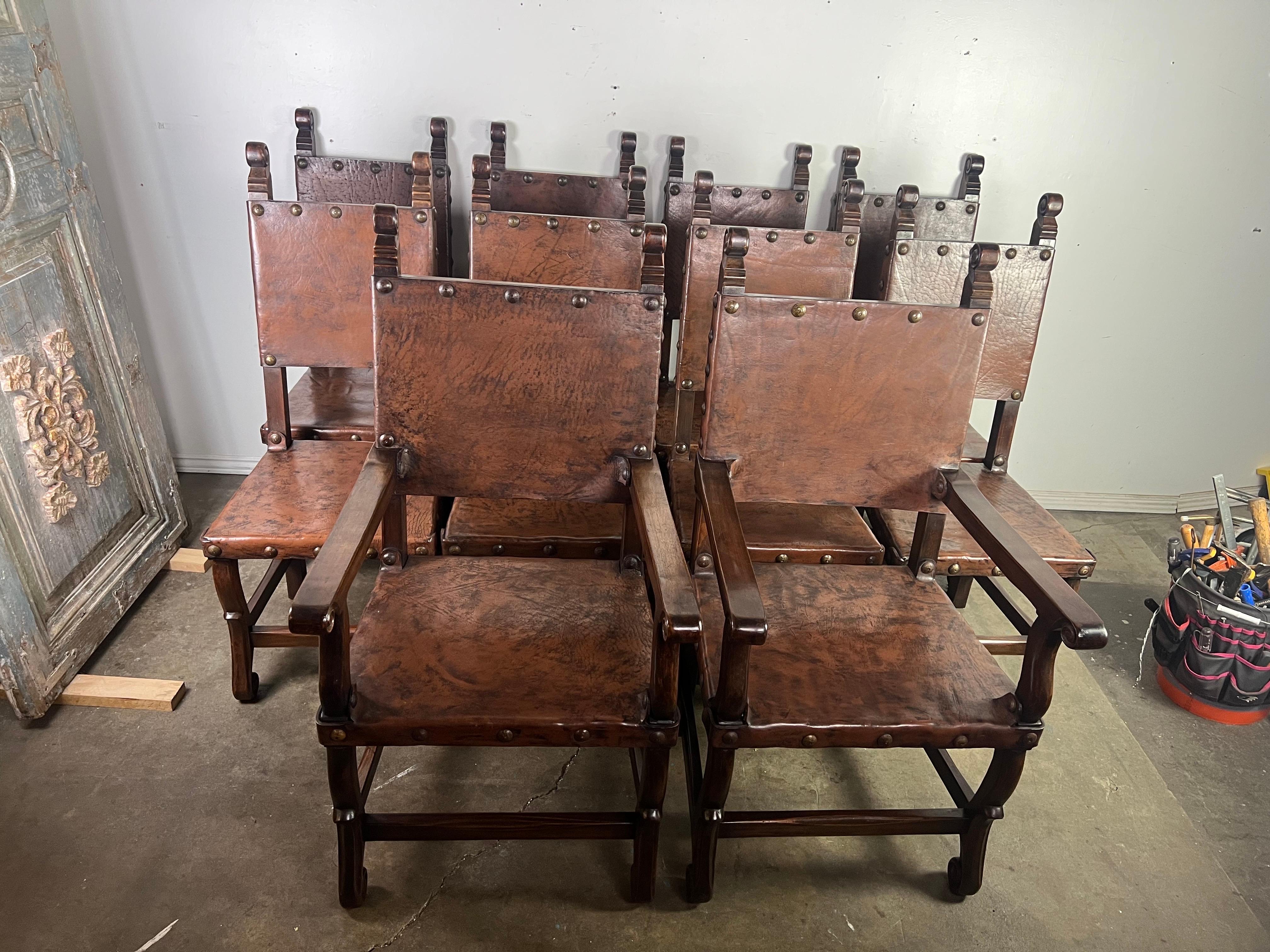 A set of ten Spanish dining chairs including two armchairs and eight side chairs with leather seats and backs.  The chairs are sturdy with a dark walnut frame and decorative turned details on the arms and backrest posts.  The leather is a rich brown