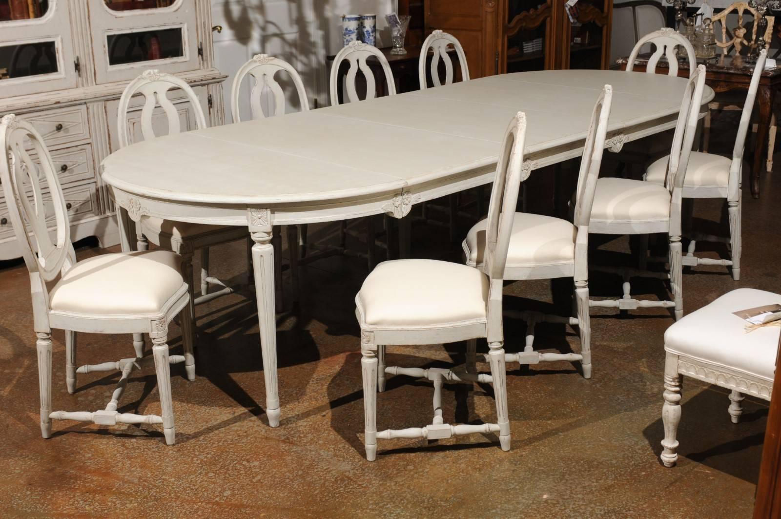 A set of ten Swedish Gustavian style painted wood dining chairs from the early 20th century, with oval pierced backs, fluted legs, cross stretchers and new upholstery. Each of this set of ten Swedish dining room chairs features an oval back with