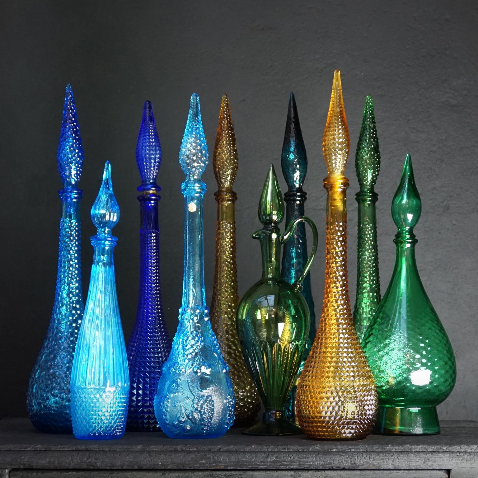 Very colorful and decorative set of ten glass 'genie in a bottle' decanters with different glass motifs and colors. 

All bottles have their stopper and are different in color, design, shape and size (height with stopper):

Green hand blown